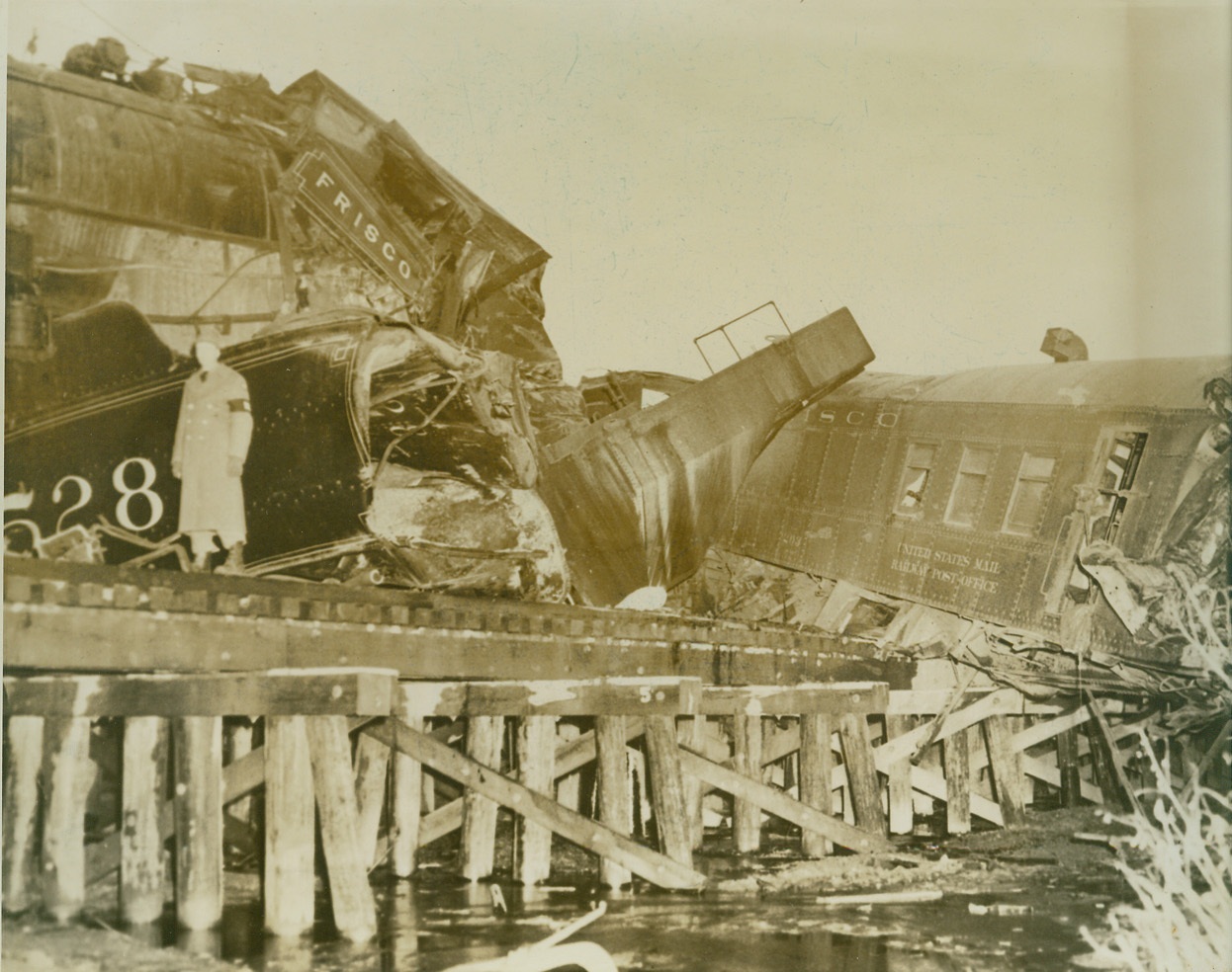 SPECIAL TRAIN CARRYING TROOPS IN HEAD-ON CRASH, 3/7/1942. GRANBY, MO. – Seven persons were killed and at least forty-five were injured when a special train carrying troops and a fast Frisco passenger train, the Will Rogers, collided head-on in the middle of a trestle at Granby. Four of the dead were soldiers who were among 230 recruits enroute from Camp Grant, Ill. The other three were crew members on the Will Rogers. Railroad officials said a mix-up in signals was responsible for the head-on collision. Passed by Army censor. Credit: ACME;