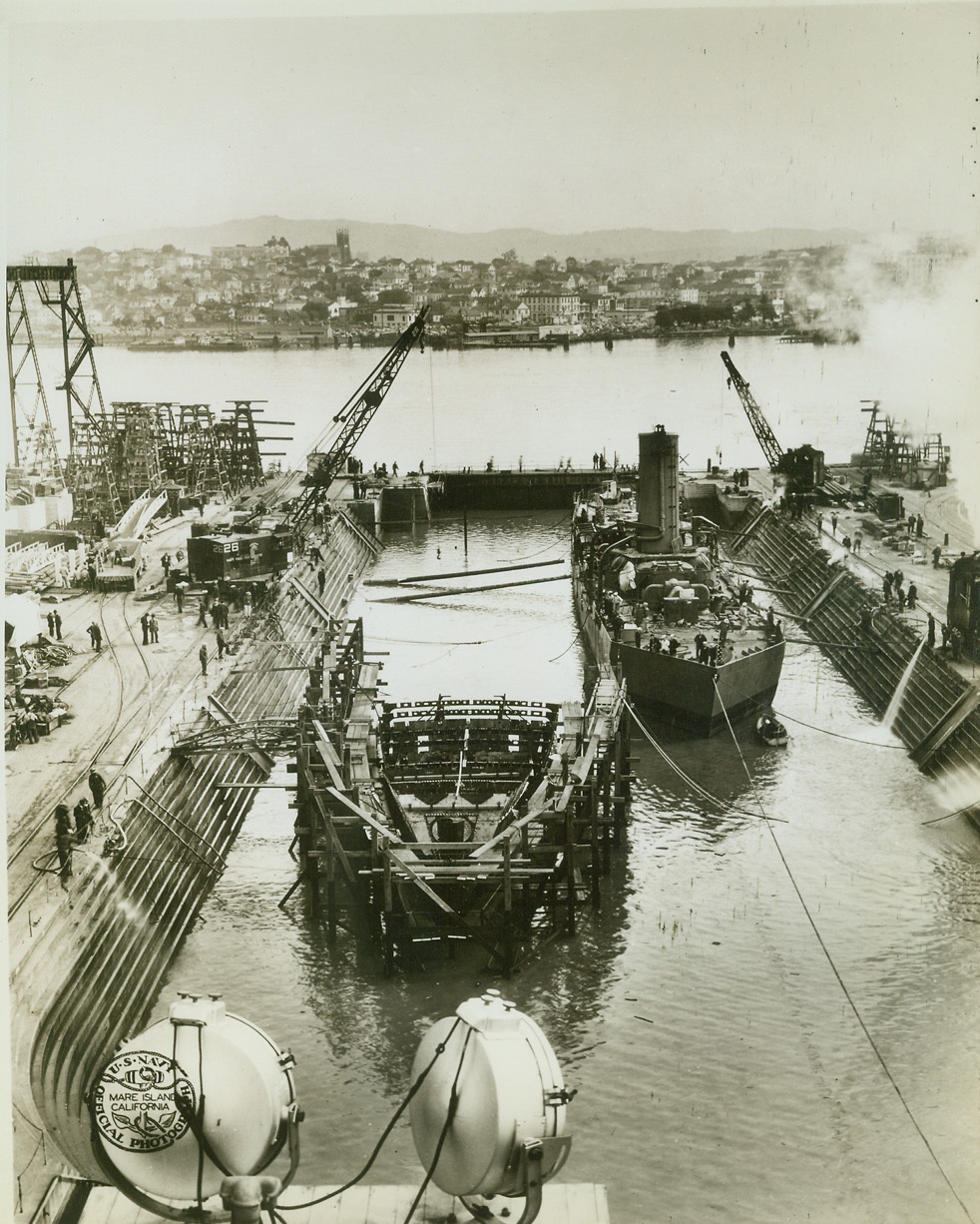 USS SHAW TAKES A BOW, 3/9/1942. AT A PACIFIC COAST NAVY YARD – The destroyer USS Shaw, badly damaged in the Dec. 7 attack on Pearl Harbor, is shown being floated into drydock for the removal of her temporary bow and the addition of her new forward section, shown in left foreground. The temporary snub bow was fitted onto the Shaw after the vessel was blasted at Pearl Harbor. She reached the mainland under her own power. Credit: U.S. Navy photo via OWI Radiophoto from ACME;