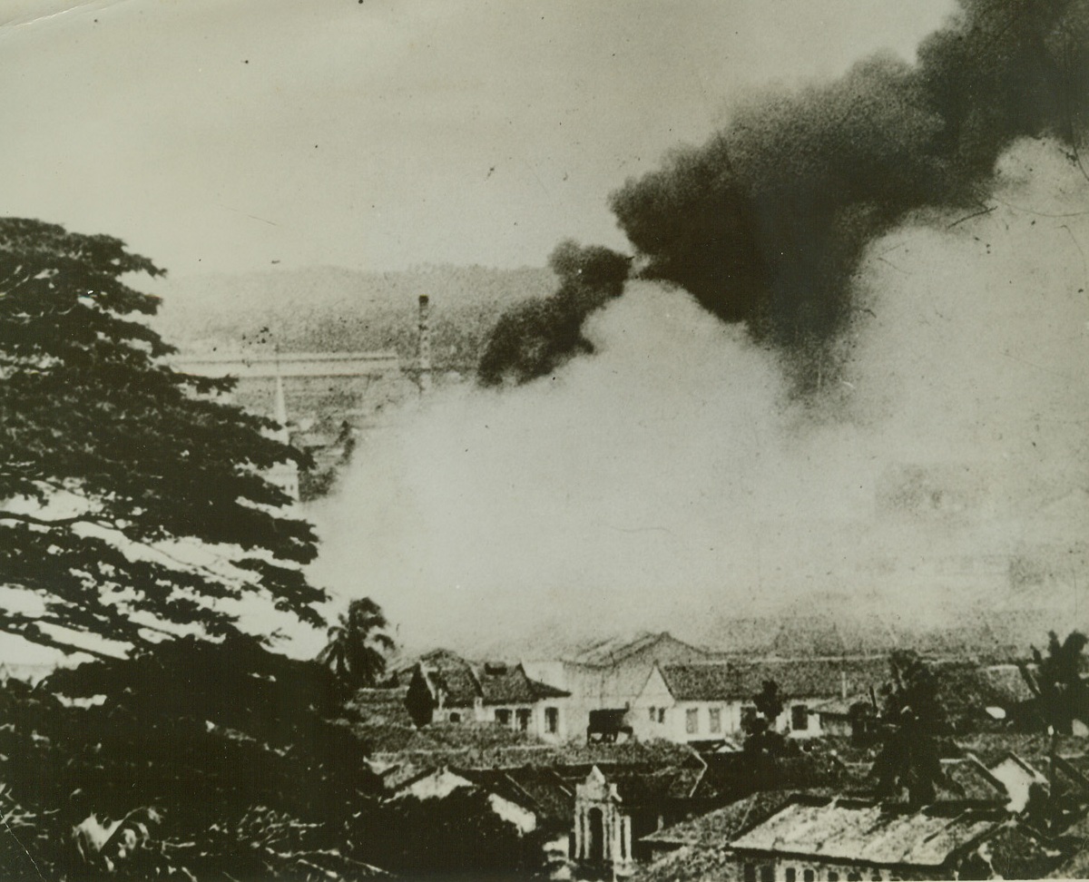 Singapore Blazes as Japs Move In, 3/17/1942. Singapore, Malaya – One of the last pictures to be made of beleaguered Singapore, this shot shows a huge column of smoke rising from countless fires created by Japanese incendiary bombs. Credit line (ACME);