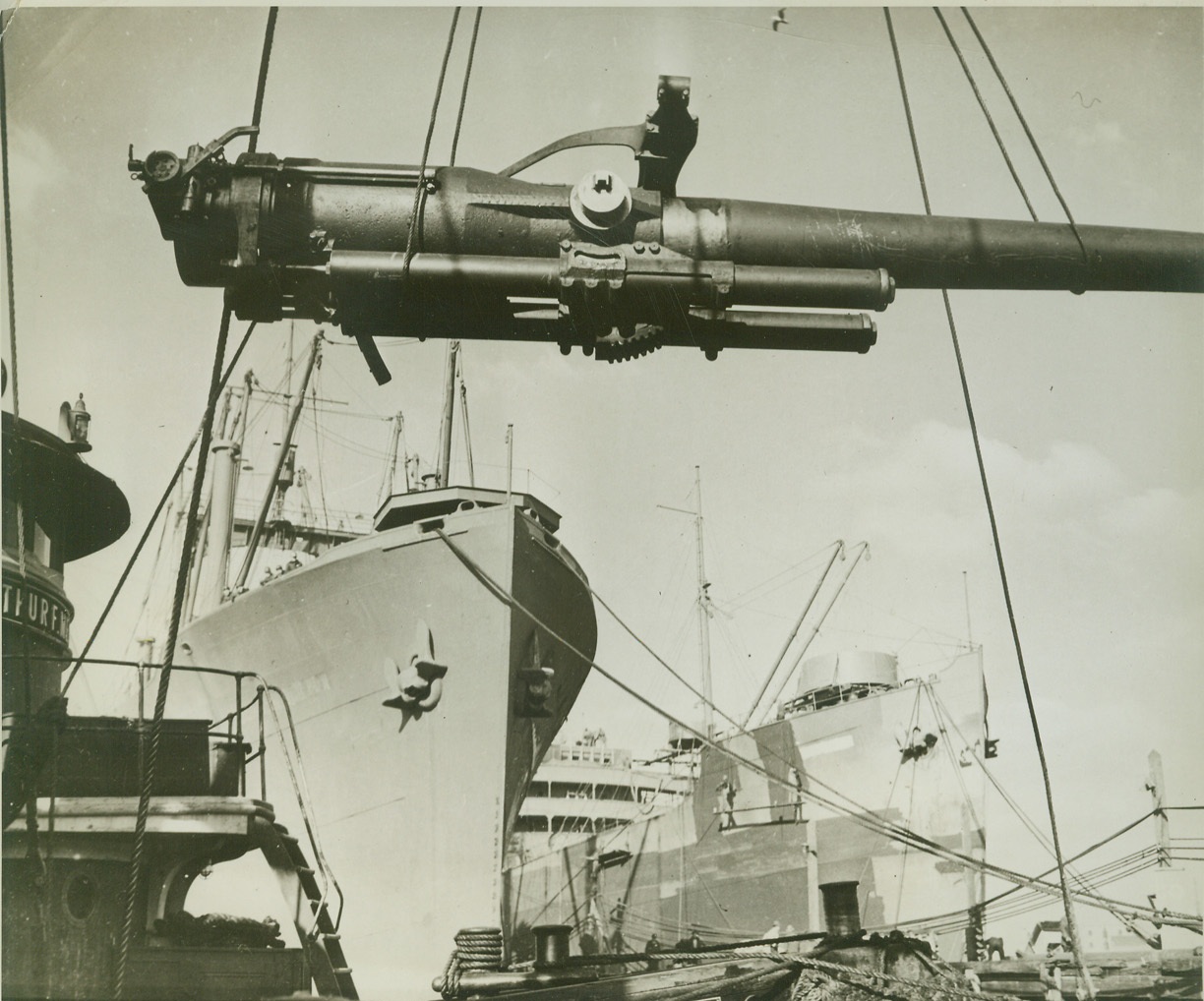 Navy Speeds Arming of Merchantmen, 4/9/1942. Heavy gun, as it is hoisted aboard a merchantman by a powerful crane, in a shipyard “somewhere in the United States.” Credit: Official Navy photo from ACME.;