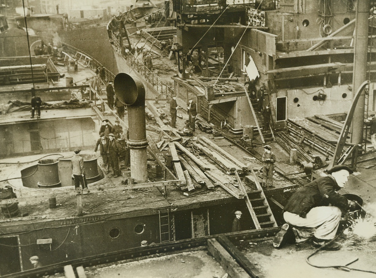 BUILDING SHIPS FOR THE BRITISH MERCHANT NAVY, 4/2/1942. AN ENGLISH PORT – British shipyards are launching ships with all possible speed; a 10,000-tonner now gets its last coat of paint only five and one-half months after the keel laying.  Widespread use of pre-fabrication has helped this speed-up and welding instead of riveting saves time and steel.  Here, work is shown in progress on the decks of almost completed ships at a shipyard at “an English port”.Credit: Acme;