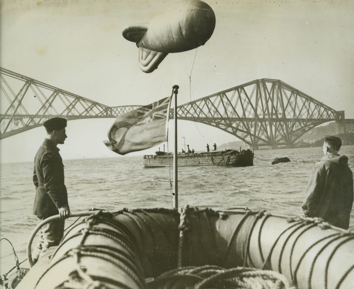 Barrage Balloon Over the Firth of Forth, 5/18/1942. FIRTH OF FORTH, SCOTLAND—Barrage balloon, as it floats over its anchor barge, part of the defenses of the Firth of Forth, where Nazi Air Force struck during the early part of the war. Famous Firth of Forth bridge can be seen in the background. Credit: ACME.;