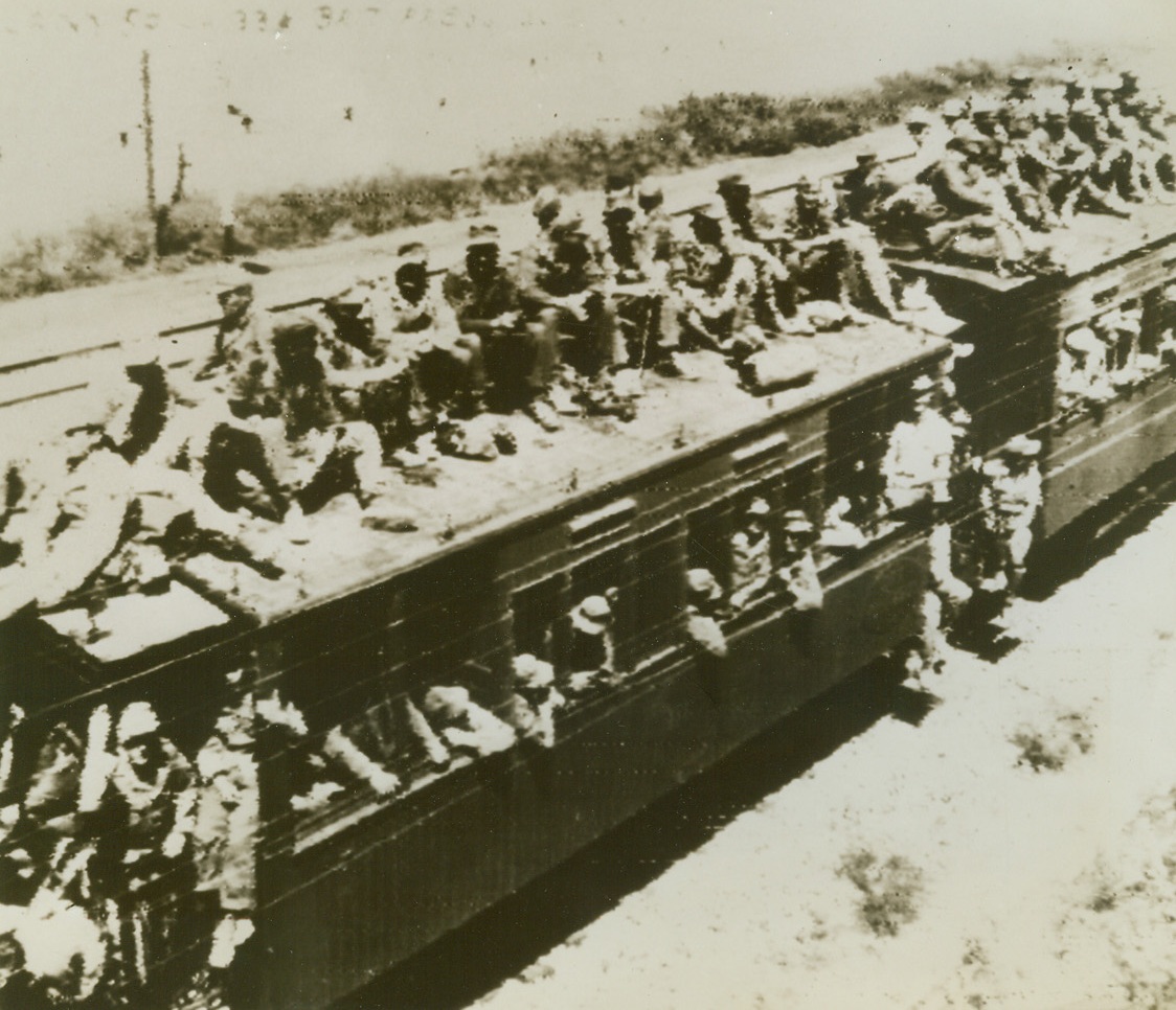 Balcony Seats Only, 5/20/1942. Tunisia – Steps, aisles, and the roof of this prisoner train are jammed with German prisoners passing through Tunis on their way to captivity.  The captured Nazis who lean out of windows see nothing but marks of their country’s defeat in Tunisia where  wrecked axis equipment clutters the landscape.  Photo radioed from Cairo to N.Y.);