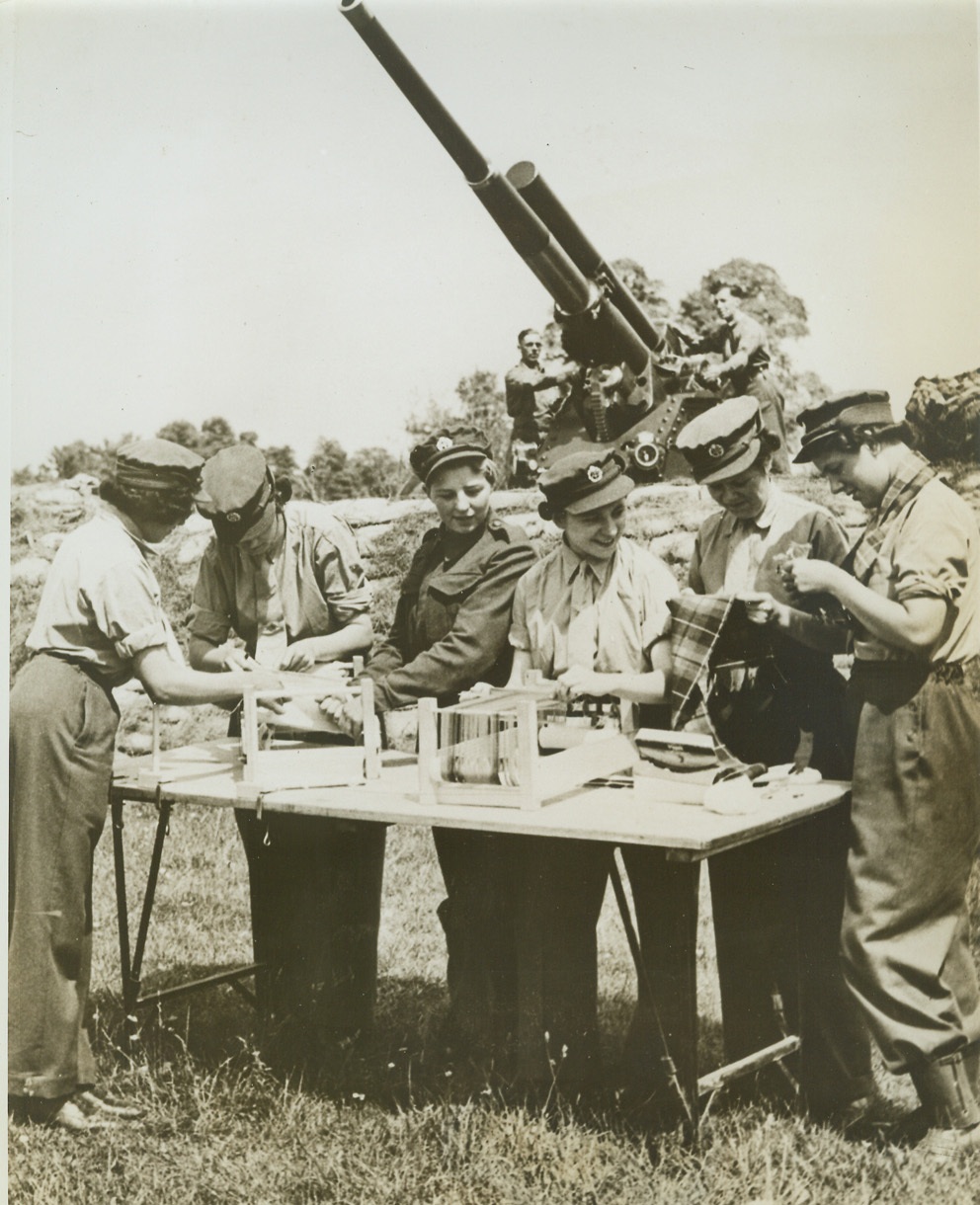 WEAVER GUNNERS, 7/28/1942. ENGLAND – In the shadow of their anti-aircraft gun, ATS girls of a mixed anti-aircraft battery in southwest England weave Scottish tartans. The girls are not Scots, and neither are their instructors, but their battery commander is, and in his honor the gunner-knitters chose the Fraser tartan for their first effort. (Passed by British censor). Credit: ACME;