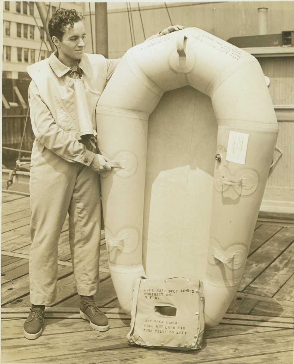 PARACHUTE BOAT FOR FIGHTER PILOTS, 7/30/1942. NEW YORK – An ingenious new one-man parachute boat, instantly inflatable, for emergency use on single-seater fighter planes is being produced by the U.S. Rubber Company. The total weight of this boat, including the eleven items of vital equipment that help protect the flier is only twelve pounds. It is attached to the pilot as a seat pack when he is in the plane. Ralph Douglas, who in a demonstration today jumped into the East River with a packed boat and in less than ten seconds had it inflated, shows a packed boat and a similar one inflated. Credit: OWI Radiophoto from ACME;