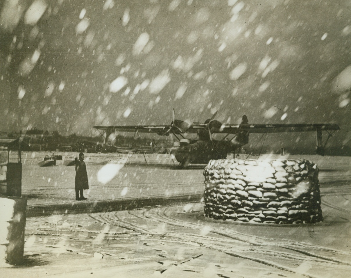 WHAT FLYERS IN ALASKEN AREA ARE UP AGAINST, 8/15/1942. Sudden snow storms are added handicaps to flying in the Northern Alaskan and Aleutian areas. Here, a Navy PBY Patrol Bomber and a “pillbox” as sandbags are almost obscured by a snow flurry. This picture describes more graphically than any words the difficulty encountered in maintaining the sky patrols in part of Alaska.Credit: U.S. NAVY OFFICIAL  PHOTO FROM ACME;