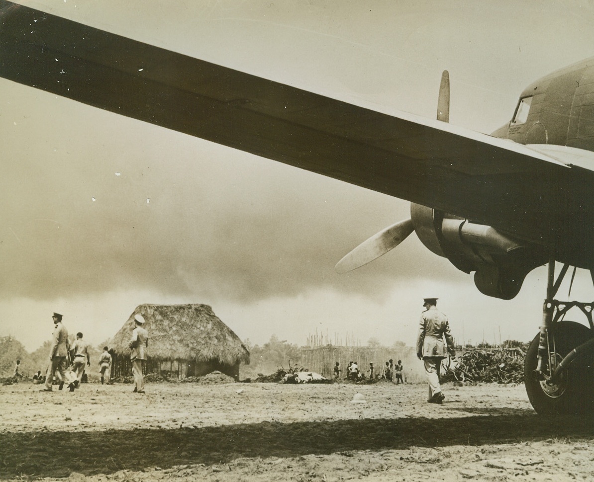 Hut in the Way of Progress, 8/26/1942. Liberia—A big modern airliner spreads its wing symbolically over a crude thatched native hut standing on a field in Liberia which Pan American Airways is converting into an airport for its proposed trans-oceanic service across the South Atlantic. Passed by censor. Credit: ACME.;