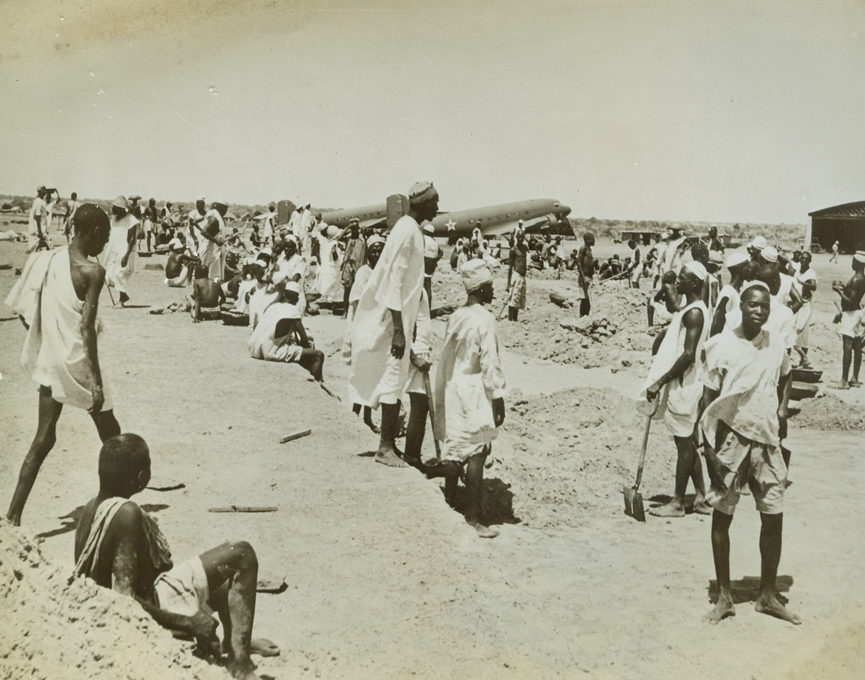 Liberian Airport Builders, 8/26/1942. Liberia—Clad in white robes, sheets, or just shorts, natives grade the earth for a new airport somewhere in Liberia which Pan American Airways is building for its proposed trans-oceanic service across the South Atlantic. Passed by censor. Credit: ACME.;