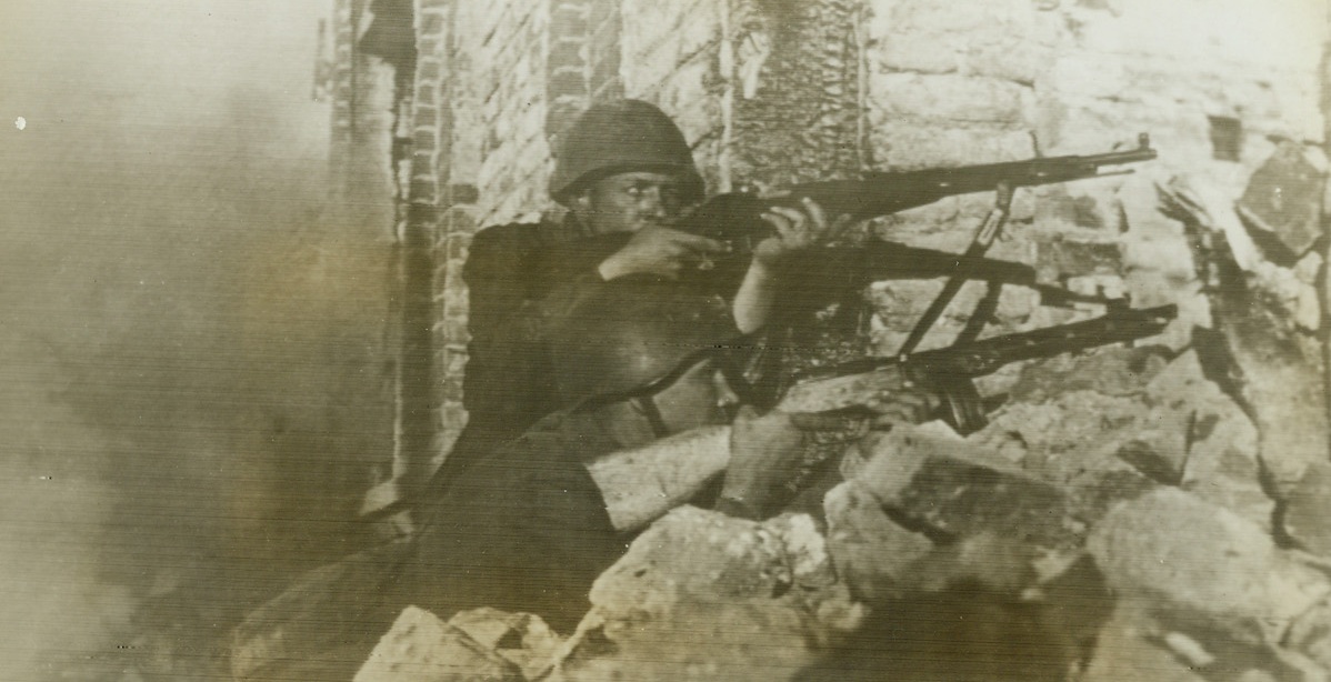 Driving Germans Out of a Russian Town, 8/30/1942. Soviet-German Front—A Soviet rifleman and submachine-gunner dislodge Germans from shelters during street fighting in a town in the Pogoreloye-Gorodische area on the Rzhev front as the Nazis get out of town under a Red Army offensive. Photo was flashed from Moscow to New York today by radio. Passed by Soviet censor. Credit: ACME radiophoto.;
