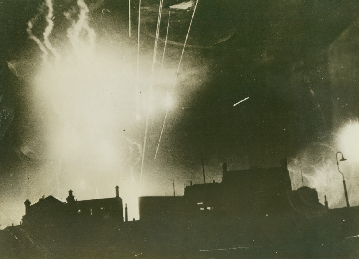 Weird Lighting During Night Raid, 8/27/1943. England – This night picture, taken during a raid on a South coast town recently, shows the weird effect caused by flares when they are hit by anti-aircraft gun fire as disintegrated parts of a flare descend over roof tops. The flare on the right has just been hit. Passed by censors. Credit: ACME;