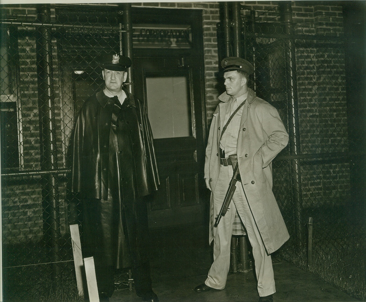 War Plant Closed by President, 8/13/1942. Bayonne, N.J.—Sgt. Charles Robinson, (left), of the Bayonne Police, and Pvt. John Glowacki, at the entrance to the General Cable Co. Plant on West First Street in Bayonne. Pvt. Glowacki accompanied Army officials, who visited the plant after President Roosevelt’s order that the Navy take over the plant had been announced. The factory manufactures cables for the Armed Forces. Credit: ACME.;