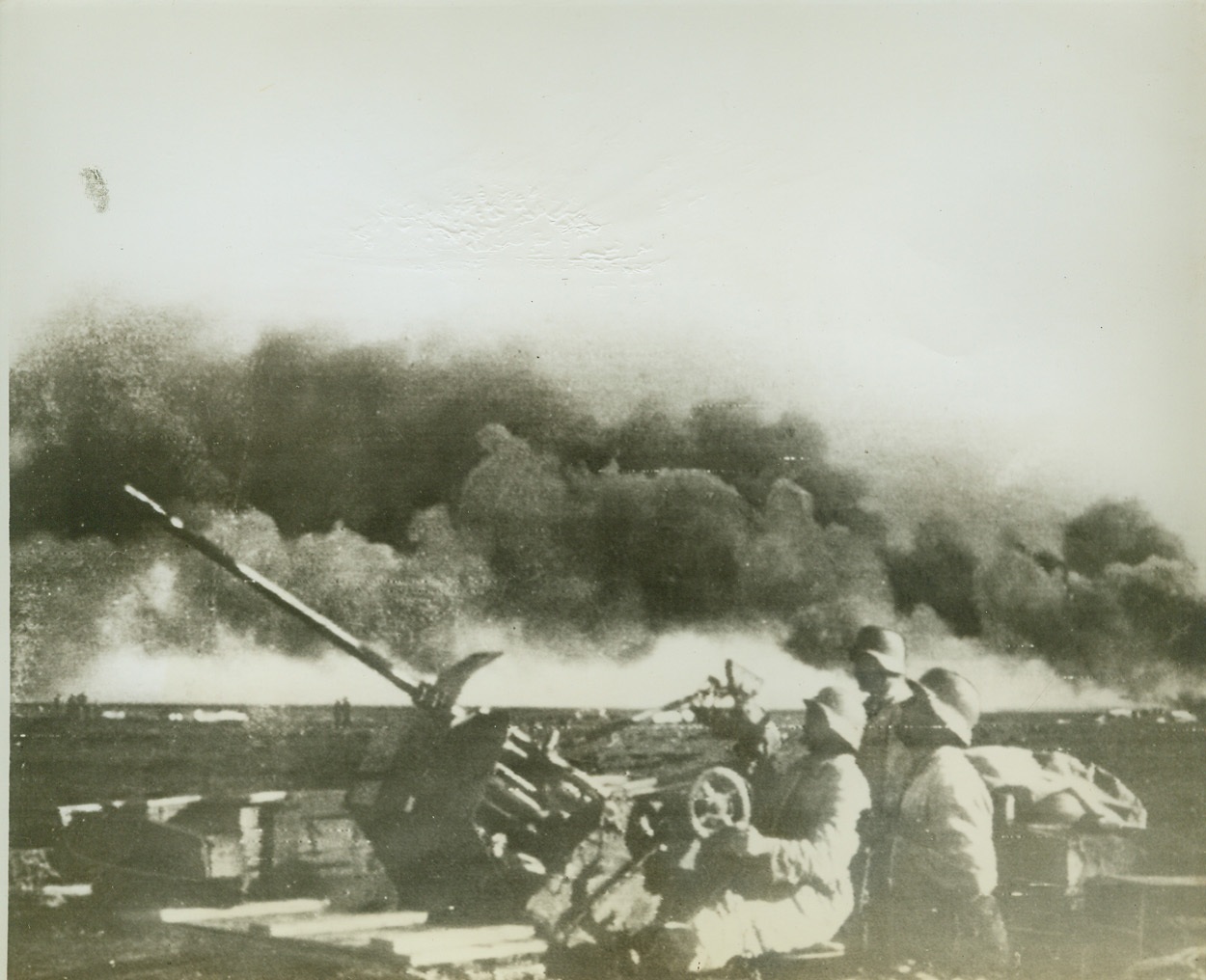 KAMPF IN AFRIKA, 8/4/1942. A Nazi anti-aircraft crew at a German air field in the Western Desert scans the sky worriedly for Allied bombers as thick black smoke from blasted Nazi planes stains the sky. Snapshot was made by a German soldier. Next day he was captured along with his camera and rolls of films. Picture was flashed to New York from Cairo today by radio. (Passed by British censor.) Credit: ACME Radiophoto;