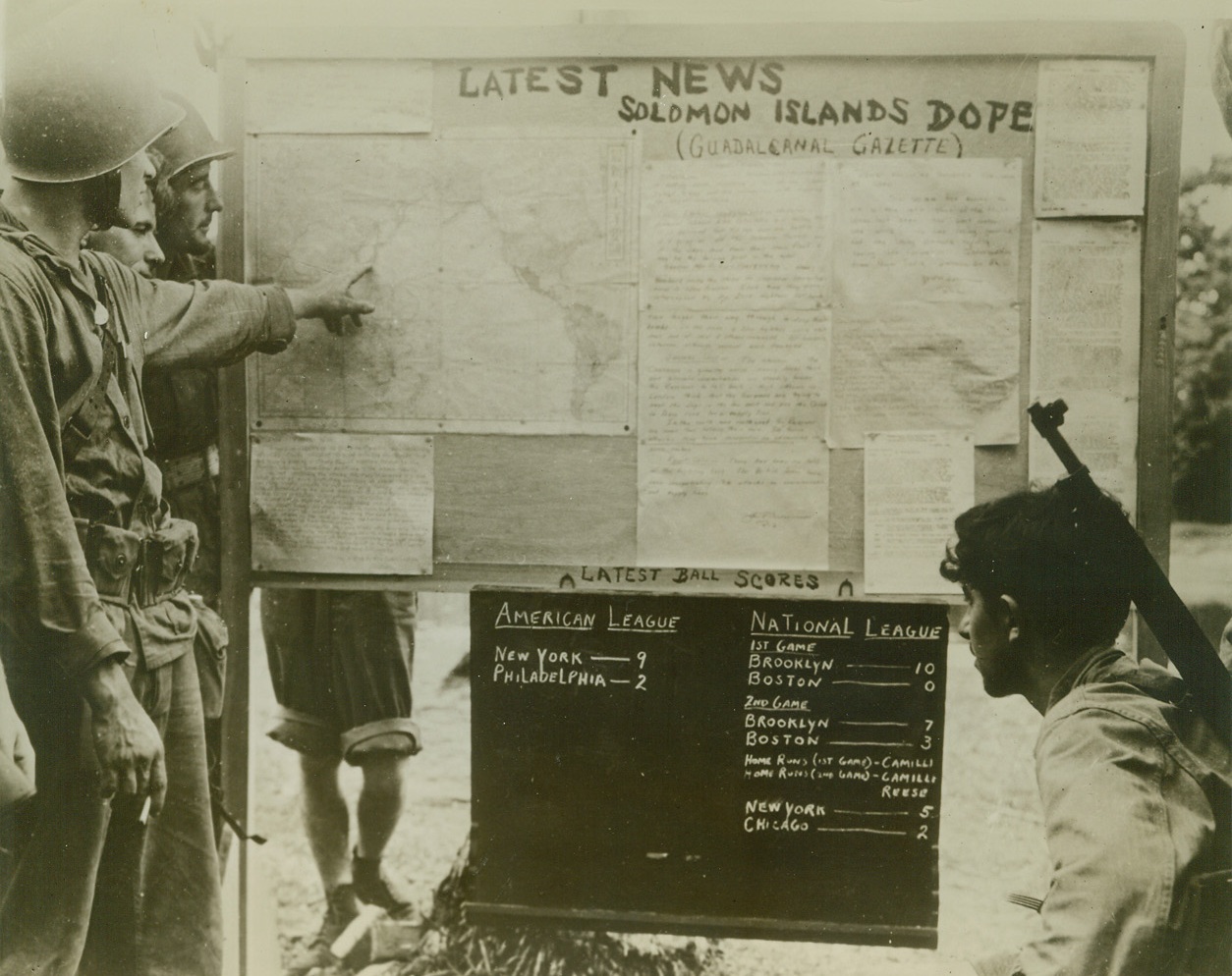 “Wuxtry! Wuxtry! Read All About It”, 9/24/1942. Guadalcanal, Solomon Islands – Marines in Guadalcanal not only make hot news for the rest of the world, but manage to keep up with the news from other parts of the world with the “Guadalcanal Gazette.”  Three of the Leathernecks locate their next goal – Tokyo, while another lad, (right), gloats over the twin victory of “Dem Bums” from Brooklyn. Credit line (U.S. Navy photo from ACME);