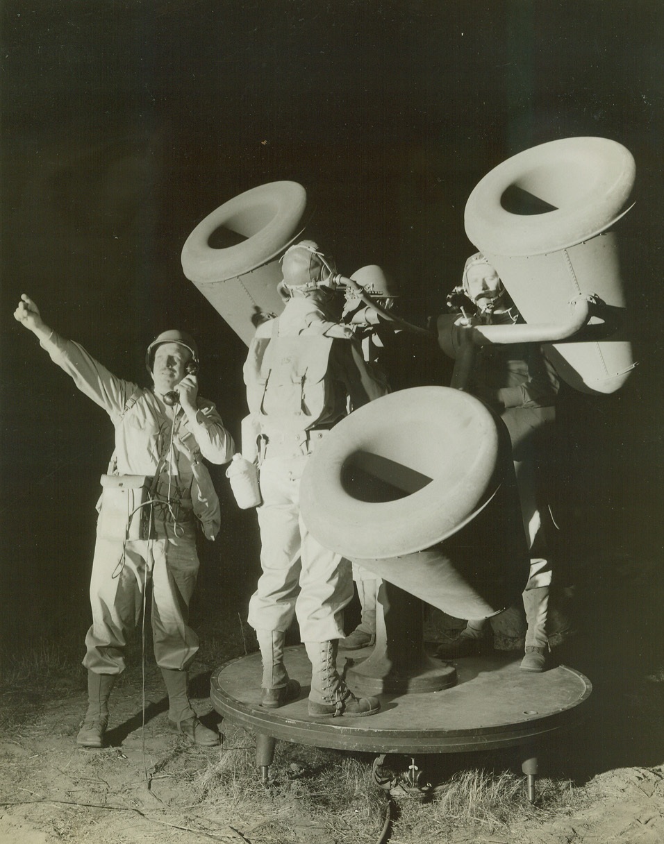 Night Plane Detectors, 9/29/1942. California—The sound detector crew of anti-aircraft coast artillery group operate their big instrument as it picks up the drone of aircraft motors during a practice demonstration in the California desert. The soldier with the portable telephone is the communications man, who reports the position of the plane to the field communications switchboard.Passed by Army censor.Credit: ACME.;