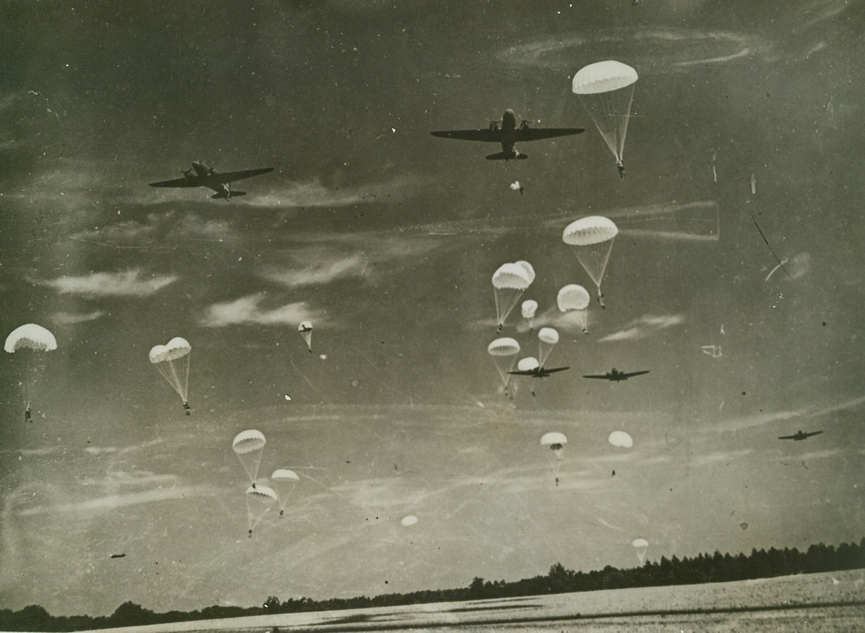 American Confetti, 9/27/1942. Somewhere in England – A ground level camera shot shows the low altitude dared on operational jumps, as American paratroops, whose presence has just been announced in England, practice invasion tactics. This is one of the first photos to show American paratroops in action. Drawn mostly from the southern states, the sky commandos are commanded by Lieut. Edson D. Raff, New York City. Passed by censor. Credit: ACME;