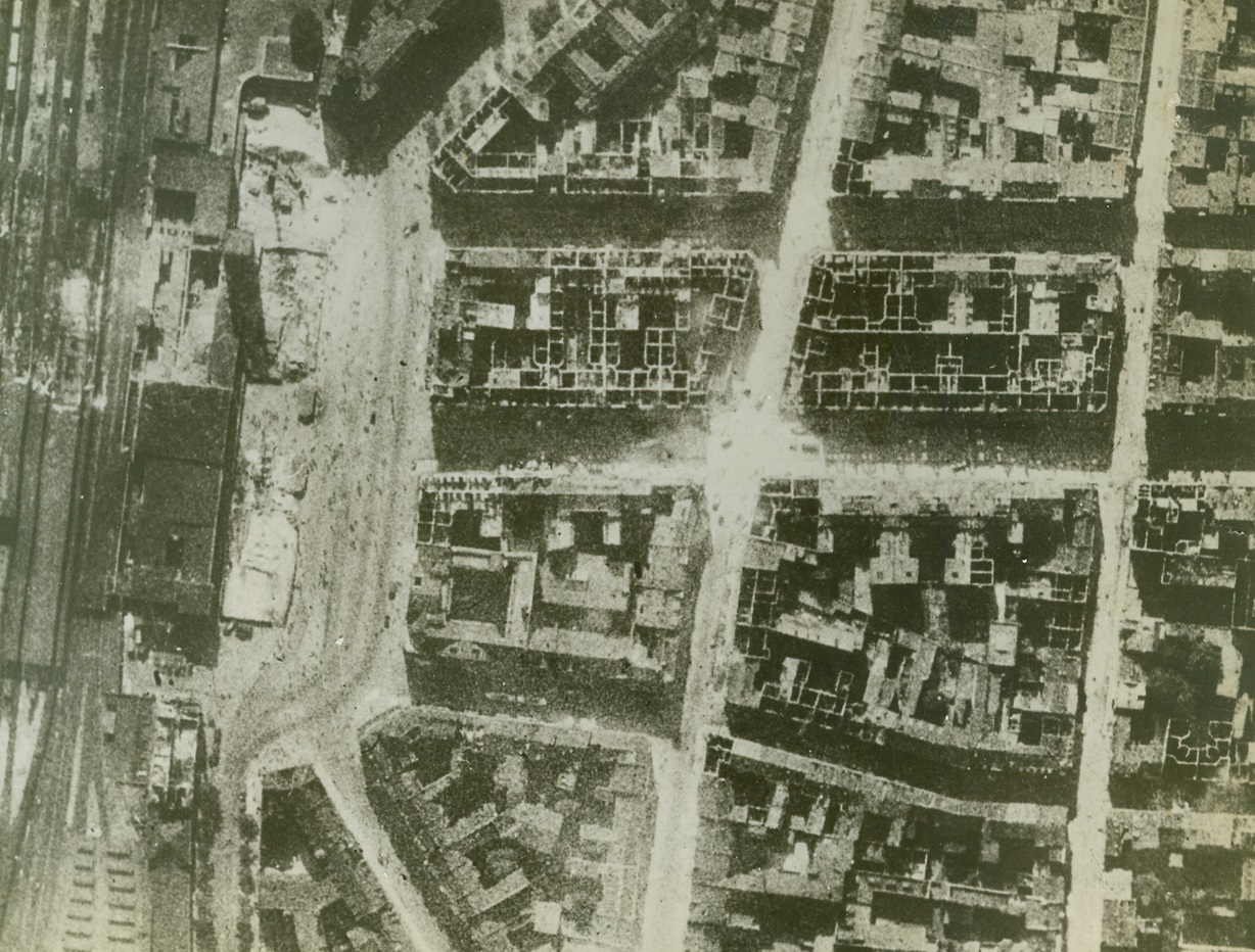 R.A.F. Bombs Blast Dusseldorf, 9/27/1942. England—A hundred yard diameter hole marks damage done to the Dusseldorf main railway station, where the main track and sheds were also blasted by R.A.F. bombs, the night of Sept. 10. Few roofs are left on buildings west of the station. The day following the night raid, thick smoke from still-burning fires made a damage estimate impossible. When the smoke cleared, this R.A.F. reconnaissance photo showed that British aim was accurate. Passed by censor. Credit: ACME.;