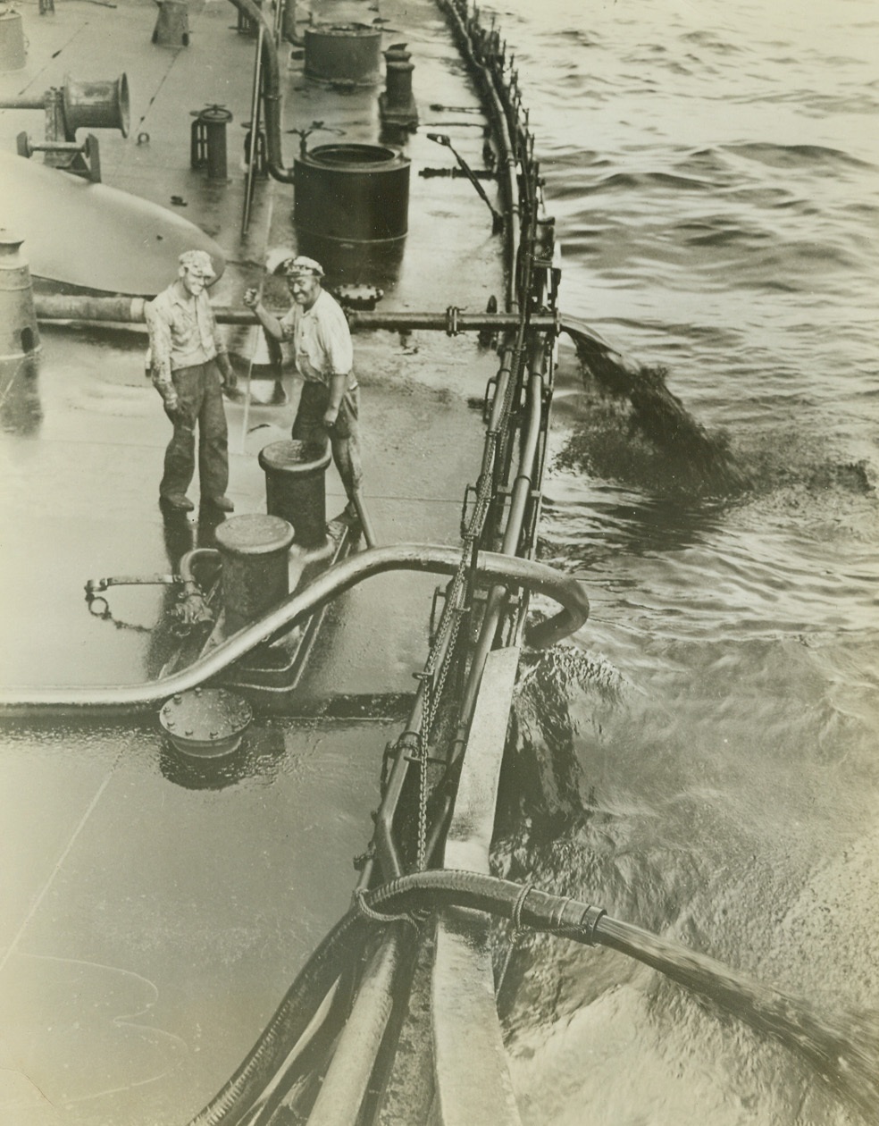Saga of the Atlantic, 9/28/1942. Somewhere in the Atlantic – After being torpedoed by an Axis submarine, seamen, in order to keep the ship on even keel after the fire, pump oil out of the ship to spread itself in the vast expanse of the ocean. Note the clenched fist of the seaman on the right—another indication that the American Merchant Sailors are determined to carry on. Credit: Official U.S. Navy photo from ACME For release in A.M. of September 30, 1942;