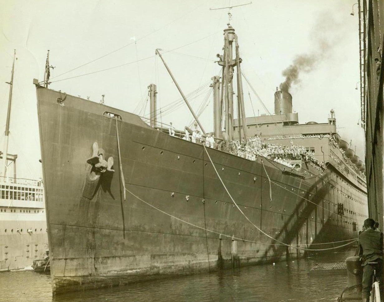 Burned At Sea, 9/9/1942. Washington, D.C. -- Abandoned on the Atlantic, after approximately 1,600 crew members and passengers were rescued, the 24,289 ton Naval Transport Wakefield, has now been salvaged and towed to an east coast port. Flames enveloped the vessel shortly after a fire of undetermined origin broke out on one of the deck levels, Sept 3. Photo shows Wakefield, in battleship gray, preparing to leave an eastern port with her load of troops;
