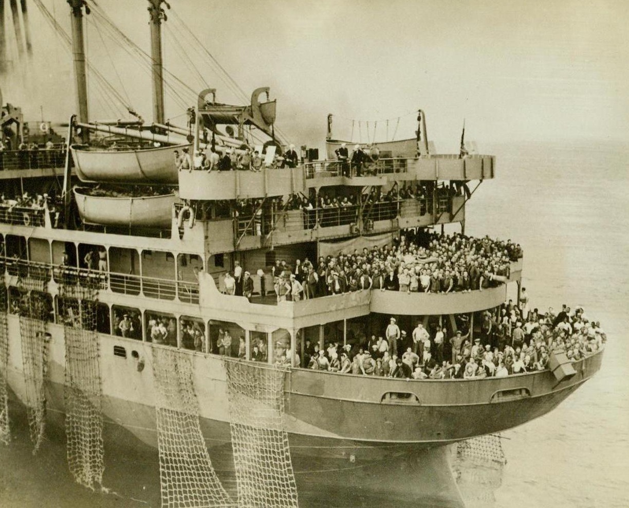 Rescue Of Wakefield Passengers, 9/9/1942. Washington, D.C. -- There is no trace of panic among these courageous passengers and crew members on the burning U.S. Transport Wakefield as they quietly wait on the stern decks of the ill-fated ship for rescue aboard the cruiser from which this photo was taken. Note rope ladders that have been let down over the sides. Orderly conduct of the survivors permitted the rescue of some 1600 persons. Though fire swept completely through the former luxury liner S.S. Manhattan the evening of Sept. 3, the vessel is reported to have been salvaged and is now safe in an Atlantic port. 9/9/42 (ACME);