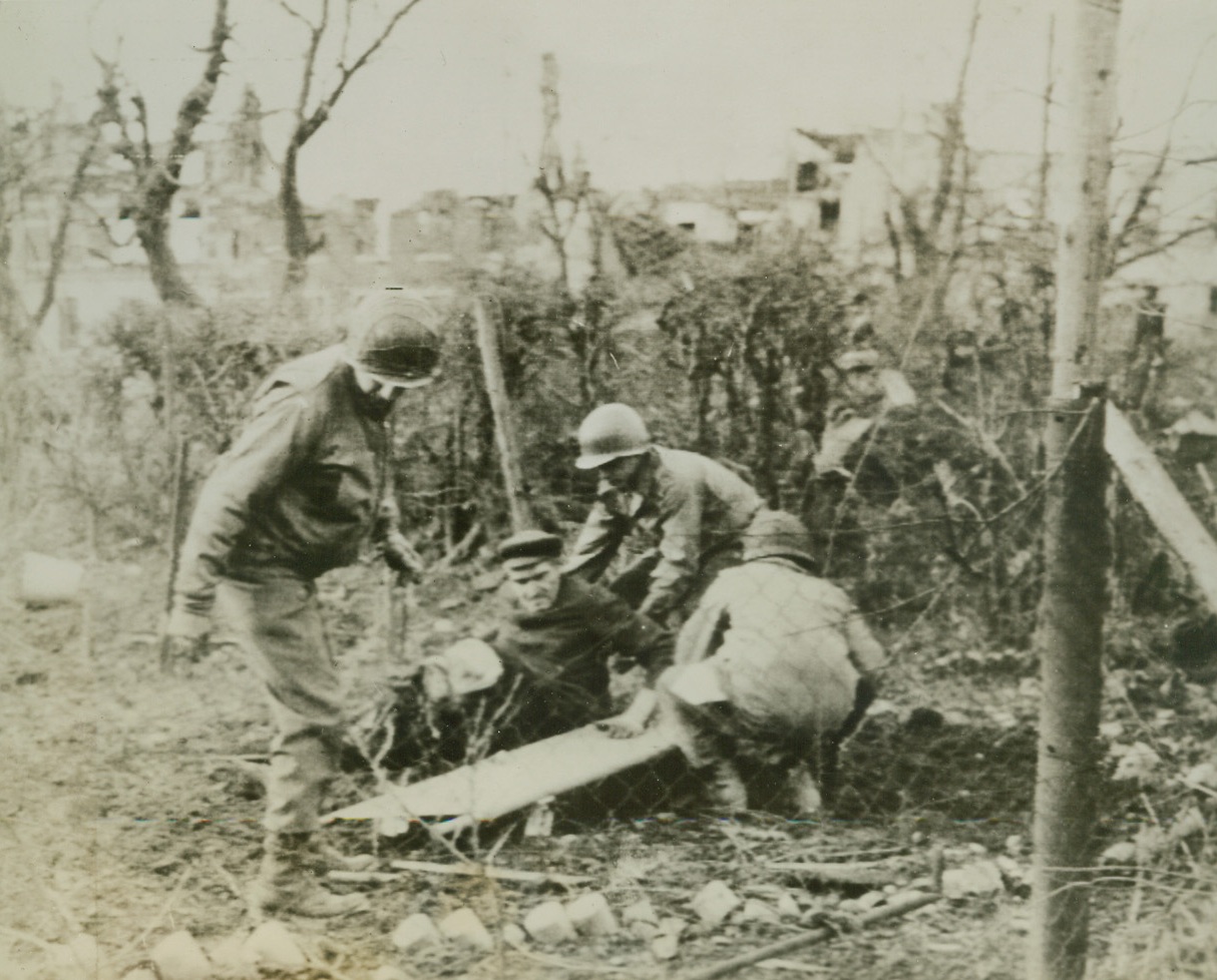 Aid Wounded German Civilian, 11/22/1944. GERMANY – A medical party in Wurselen lifts a wounded German civilian onto a litter. The civilian had just stepped on a Nazi box mine.Credit (Army Radiotelephoto from ACME);