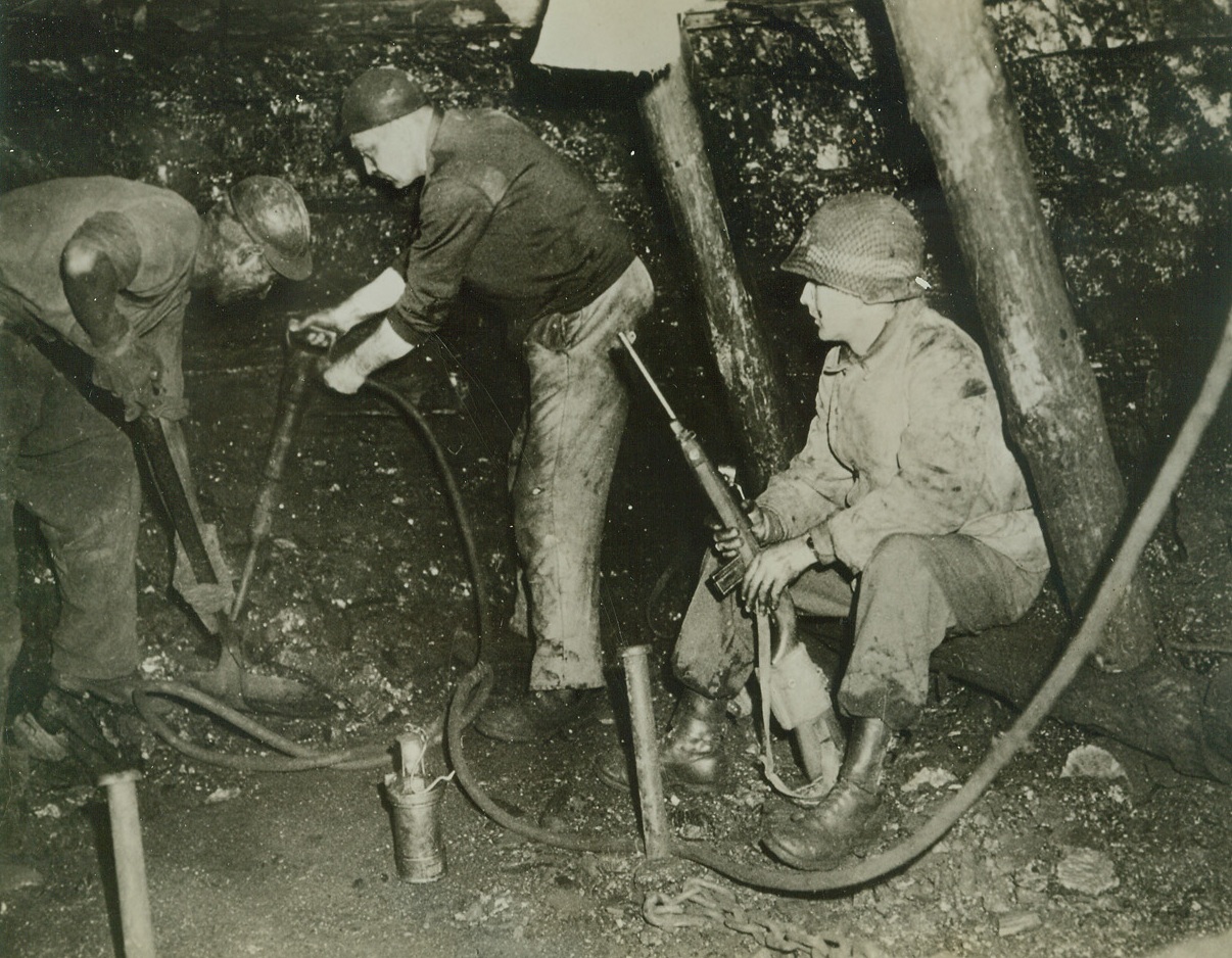 GERMANS AND YANKS OPERATE SAME MINE, 11/5/1944. GERMANY—One of the strangest incidents of this war is taking place at Alsdorf, about 8 miles northeast of Aachen, where Americans and Germans are occupying and working the same coal mine. Part of the mine is on the American side of the fighting line; part on the German side. German miners on both sides continue to get out the coal, but those on the Yank side are under constant guard. Here, Pfc. Ronald H. Meade, Toledo, Oh, watches two German miners at work in the pit. The miners are permitted to go home every evening when their shift is through.  Credit (ACME);
