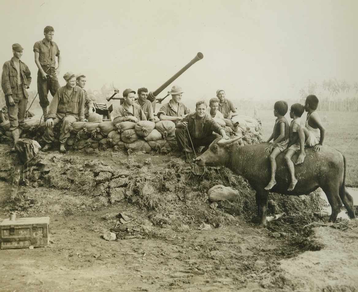 Yanks Find Out “What’s Cooking’”, 11/23/1944. Leyte Island, P.I. – During a lull in the fighting, members of a Yank ack-ack gun crew “shoot the bull” with three small citizens of Leyte island, perched atop their family’s patient caribou.  Photo by ACME photographer, Tom Shafer, for the War Picture Pool.Credit-WP-(ACME);