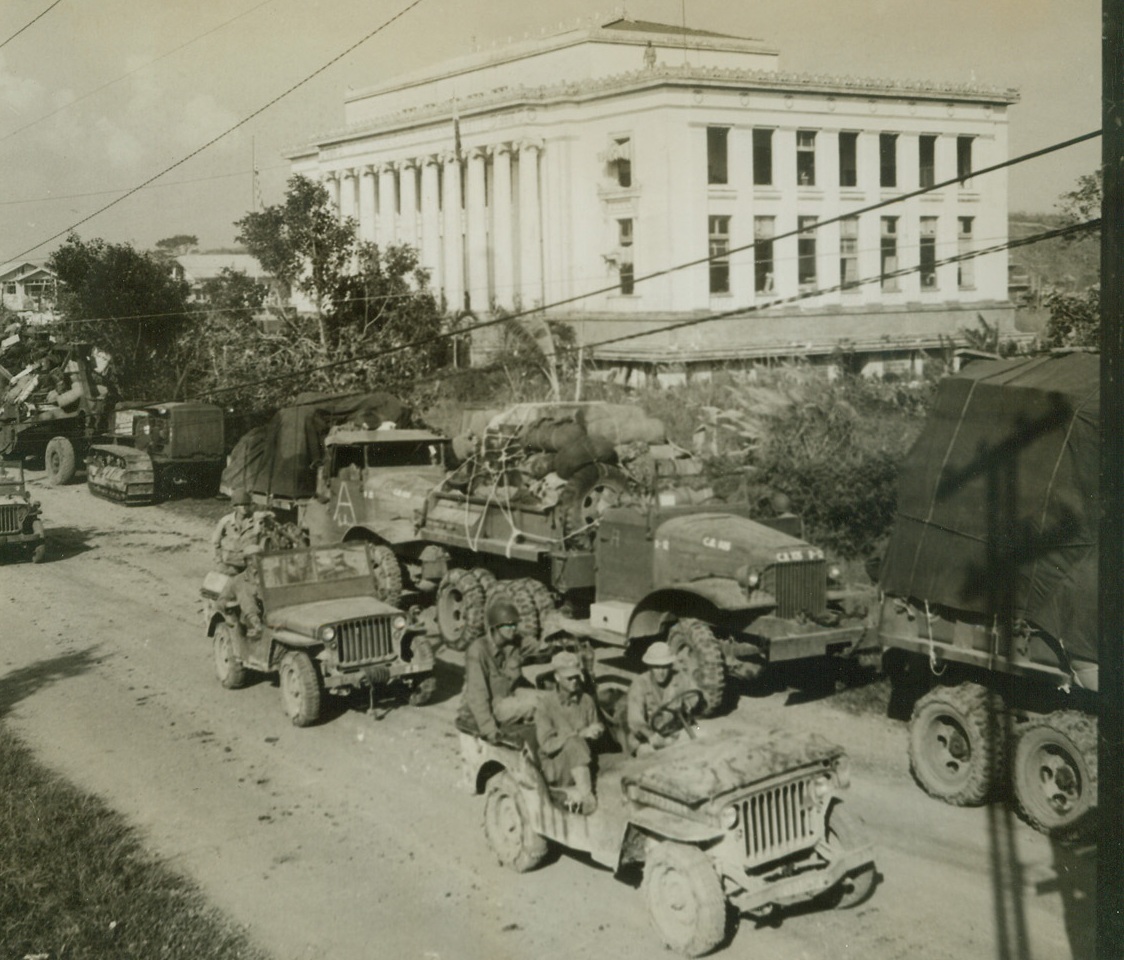 Yanks Move Through Leyte Capital, 11/5/1944. Tacloban, P.I. – As the new Philippine government begins operations in the large white capital building (background) in Tacloban, capital of Leyte, US Army supplies and equipment move through the island capital to the front lines as fighting for the island enters its final stages.;