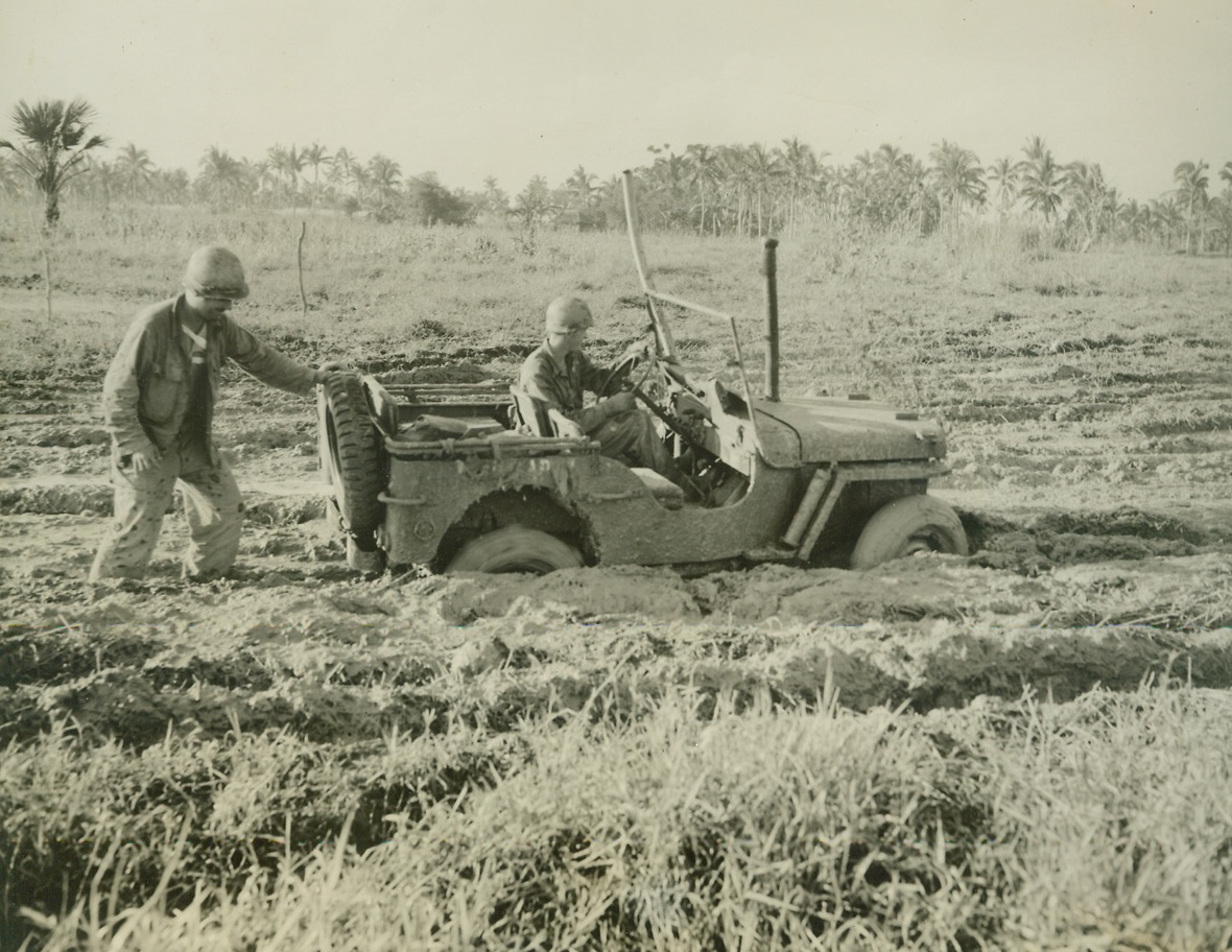 No Title. 11/6/1944. Leyte, P.I. – One of the most natural obstacles which confronted Americans as they landed on Leyte to drive out the Japs was the mud.  Thick and slimy, it bogged down mechanized vehicles and slowed the advance of the infantry.  Here, Cpl. William Stahl, Kansas City, MO., tries to drive his jeep out of a mud bog, in which he car sunk to the top of the wheels.  Lt. John A. Farnsworth, San Francisco, is pushing from the back.Credit (ACME photo by Stanley Troutman, War Pool Correspondent);