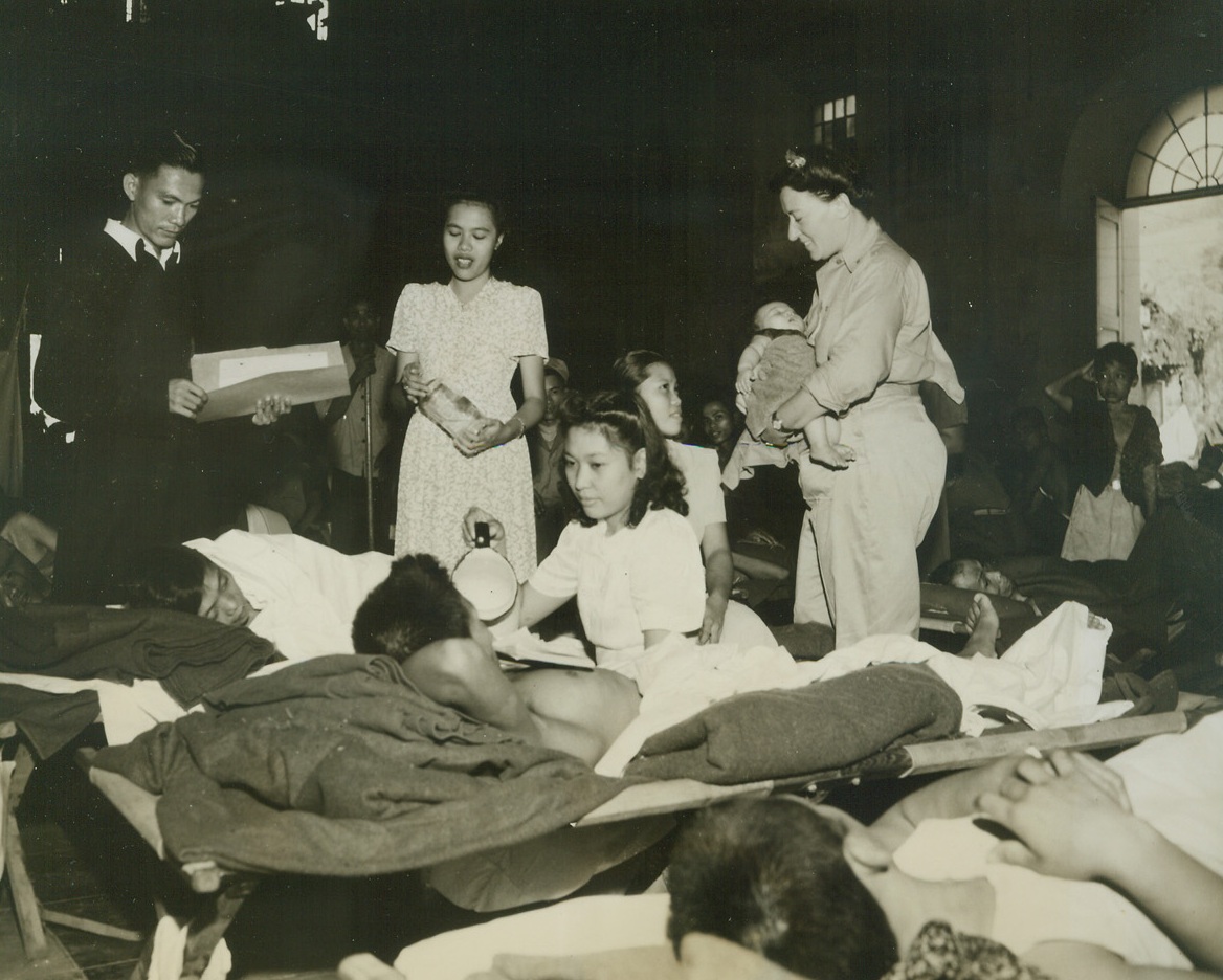 Army Nurses Give Aid Where Needed, 11/15/1944. Philippines—U.S. Army nurses in the Philippines are faced with all types of cases.  They care for the wounded, American and Filipino, tend the sick and feed the undernourished and when called upon, give comfort to the orphaned children.  Here Lt. Rose Chapman of Chicago, Ill., takes care of a native baby whose father had been brought to the field hospital set up in a Cathedral on Leyte Island.  Looking on is Father Antonio Mate, Filipino priest.  This is one of the last pictures taken by Frank Prist, Jr., ACME photographer for the War Picture Pool, who was instantly killed by a Japanese sniper bullet while cover the front in Western Leyte.Credit-WP- (ACME);