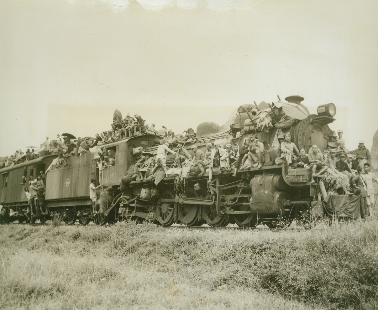 China’s Human Cargo, 11/10/1944. Eastern Front, China – Masses of humanity, united in one common purpose – flight for life—cram the railroads and highways leading from China’s Eastern front, as the instinct for self preservation sends them fleeing from Jap terror.  Simple peasants they are, familiar with only the ways of simple folk like themselves, but they know the atrocities of the Japs, rather than live under the yoke or the rising sun, they choose to suffer hardship, and even death, to evade them.  Trains leaving Liuchow are packed from the rails to the tops of the cars, and all available vehicles fill the highway as shown in this unusual and dramatic series of photos made by Frank Cancellare, ACME photographer for the War Picture Pool  On the heels of the evacuees follow constantly the fear of the dread typhus and cholera epidemic but still they go onward. New York Bureau Every inch of space on this train, from the locomotive back to the “caboose” is filled with refugees.  At one time a family of seven, riding atop one of the cars, was killed when the train entered a tunnel, and the low roof swept them off.  Photo by ACME photographer, Frank Cancellare, for the War Picture Pool. Credit-WP-(ACME);