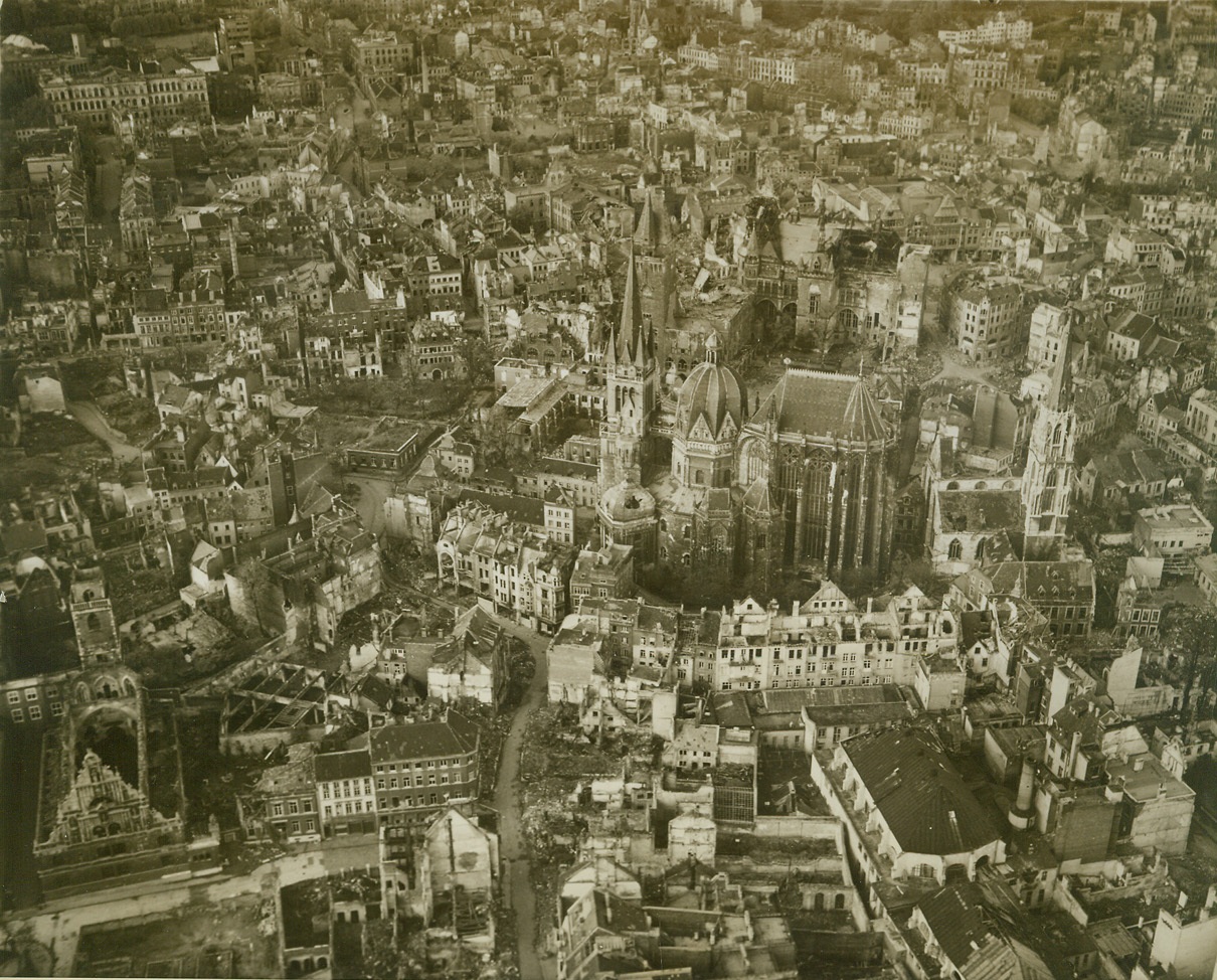 Aachen—A Dead City, 11/3/1944. GERMANY – The gutted homes and ruins of Aachen are evident in this aerial photo of the German city taken after its fall. Aachen Cathedral, burial place of Charlemagne, is the only building which stands almost undamaged amid the ruins of the city. Photo by Acme photographer, Andrew Lopez, for the War Picture Pool. Credit-WP-(Acme);