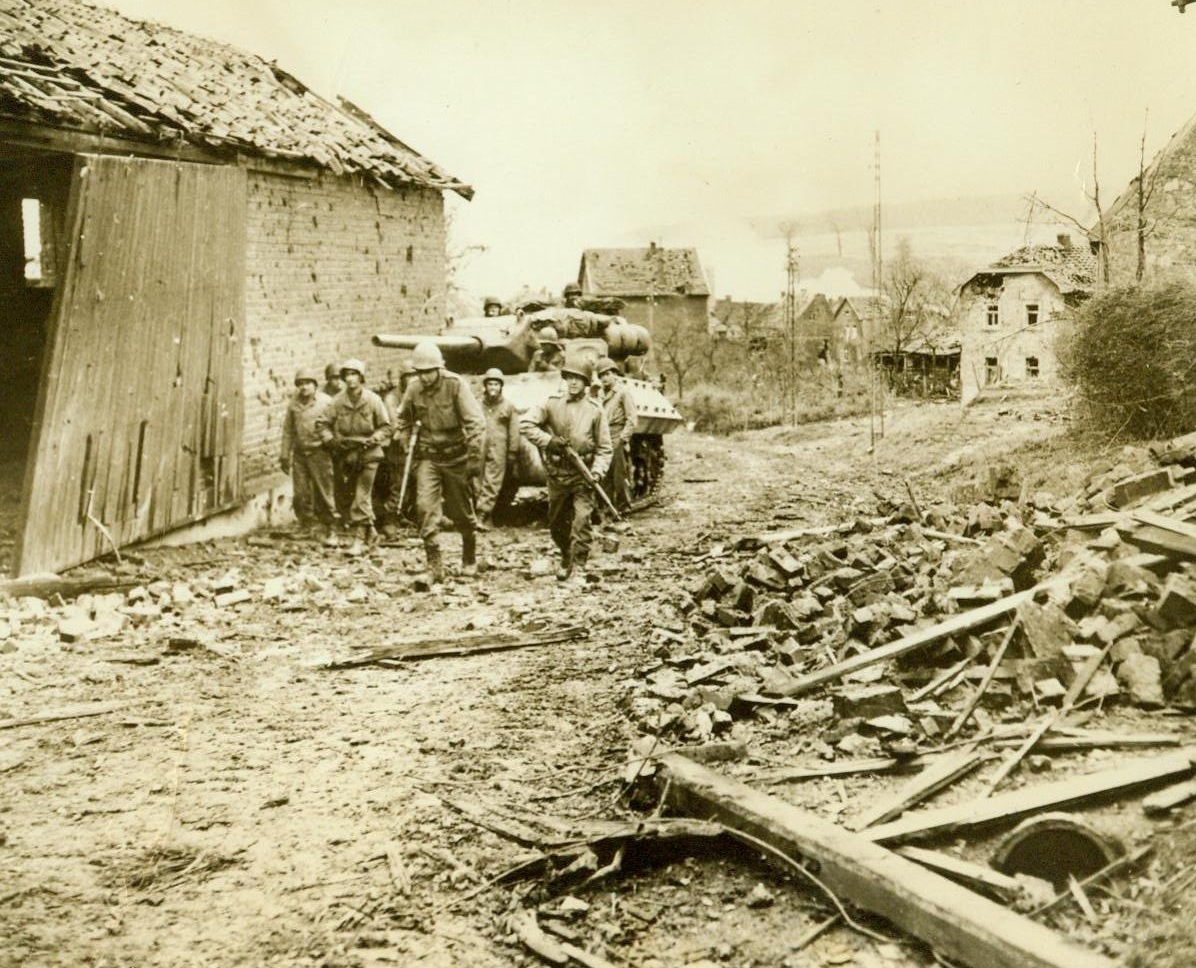 Advance In Gressenich, 11/23/1944. Gressenich, German – Trudging before a tank, Yank fighting men toil up a hill in shattered Gressenich, the first town to fall before the U.S. First Army’s new drive 11/23/44 (ACME);