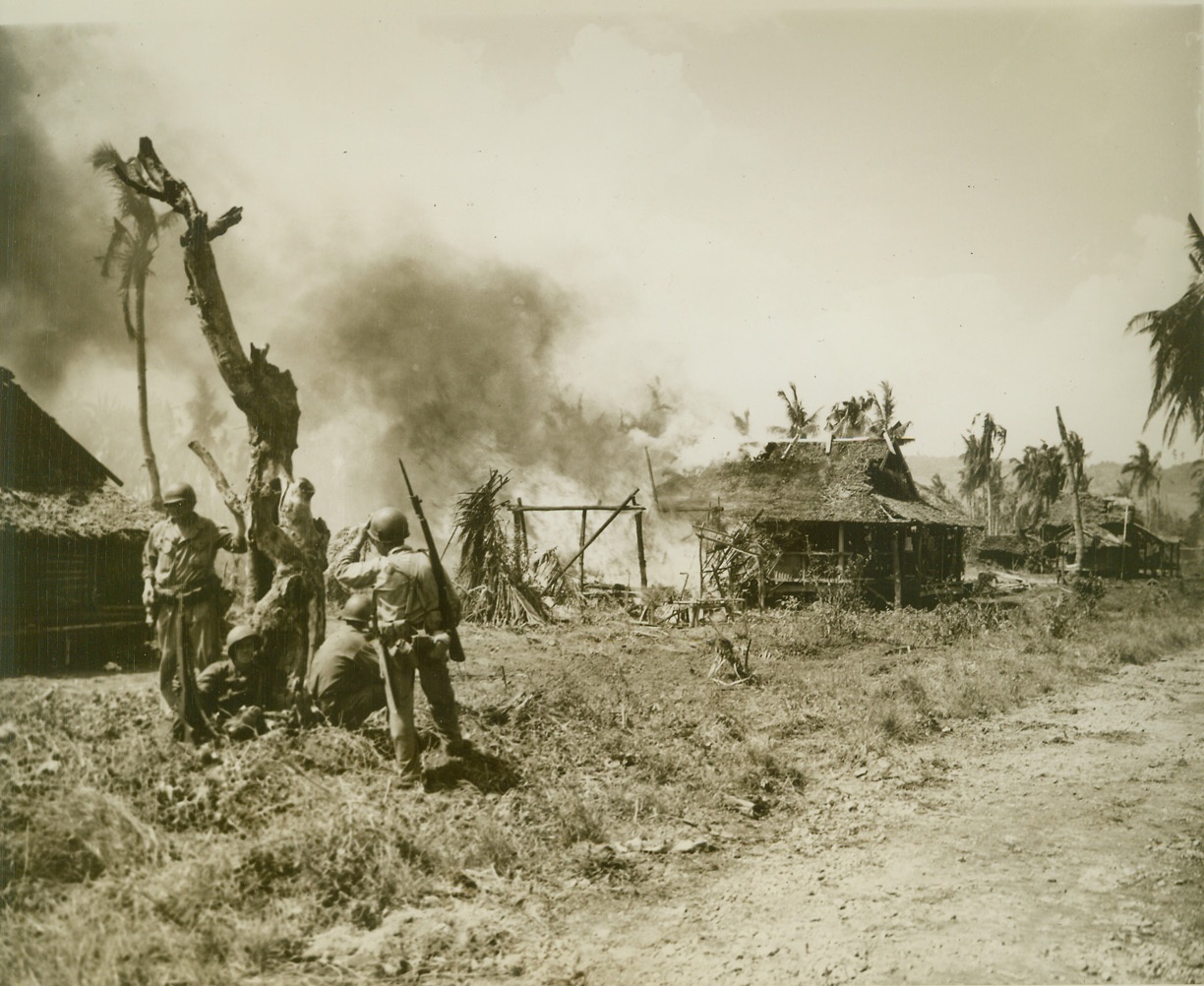 Jap Fire Razes Philippine Village, 11/1/1944. Leyte, Philippines—Infantrymen keep watch beside a gaunt, scarred tree in the flaming village of San Jose on Leyte. The tiny village caught fire as Japs sent their counter-fire toward invading Yank forces. Photo by ACME photographer Stanley Troutman for the war picture pool. Credit: ACME.;