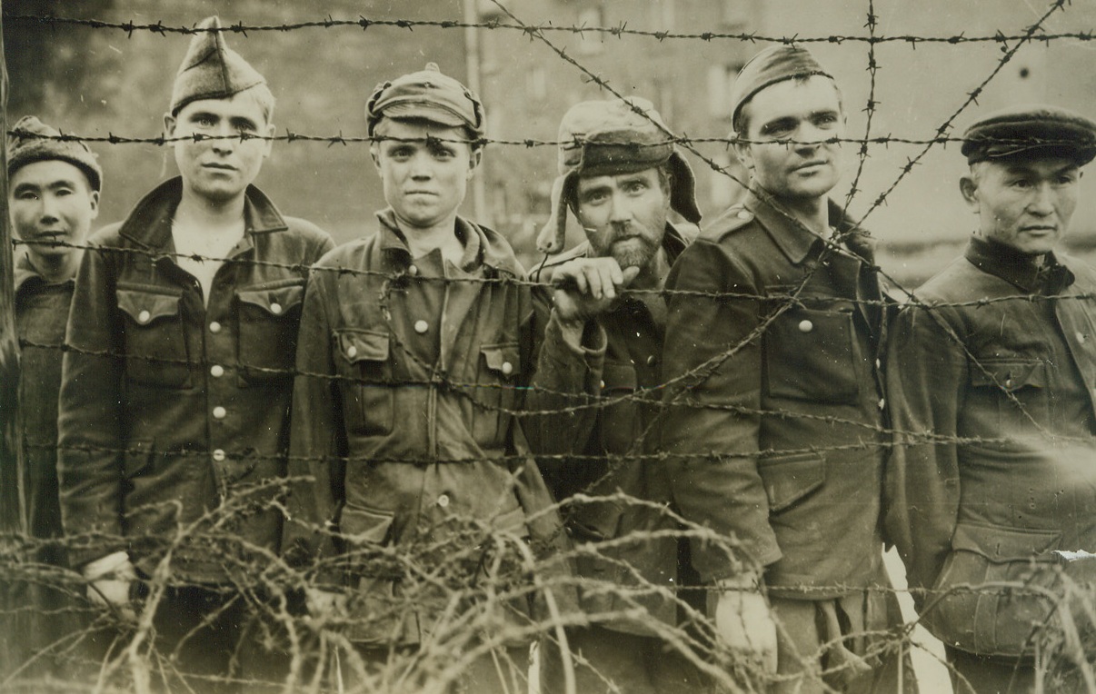Behind Wires Of A Nazi Camp, 12/20/1945. FRANCE—Prisoners look through a barbed wire fence of the former Nazi prisoner of war camp at Sarpeguemines, France, on the U. S. Third army Front.  Yanks captured the camp December 11.  Prisoners found there included about 1,000 Russians, Serbians, Italians, poles, and French, some of whom had been in German hands since the Nazis entered Warsaw more than five years ago. Credit WP ACME;