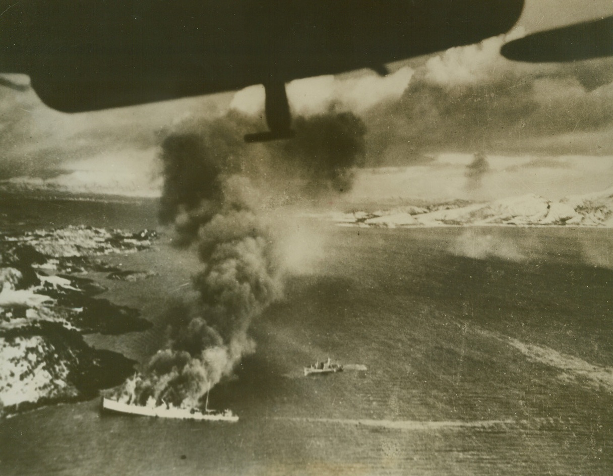 British Blast Nazi Convoy, 12/7/1944. Burning fiercely, a Nazi troop transport (left) is aground and settling by the stern, after an attack by British Fleet Air Arm Barracudas. The transport was part of a convoy of three ships escorted by an armed trawler (above, center background), caught off the coast of Norway between Mosjoen and Rorvik. All four ships were set afire and driven ashore by the attackers. Here, the trawler tires to come alongside the larger craft to rescue survivors. A few moments later it was attacked, itself. Credit Line ( British Official Photo from Acme);