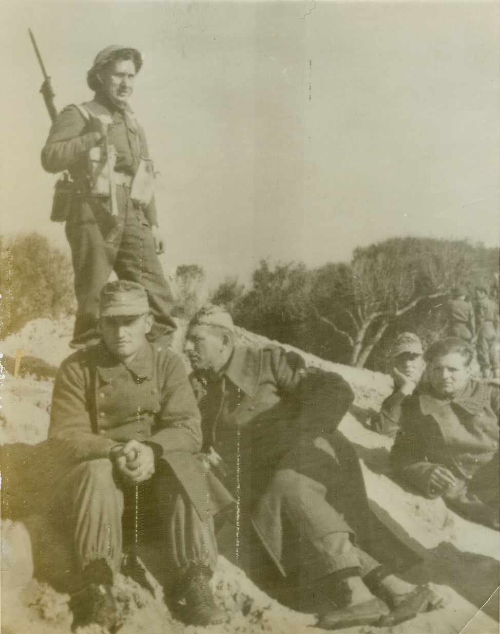 First Prisoners, 1/23/1944. With the Fifth Army in Italy – Four German prisoners, the first taken by Allied Forces after the initial surprise landing south of Rome on January 22nd, lounge on a west coast beach, guarded by a British Tommy. The entire Nazi Army was as surprised as these hapless captives to find the Allies in that section of Italy. After more than 24 hours in their new positions, our forces have met with only token resistance. Credit: British Army photo via OWI Radiophoto from ACME;