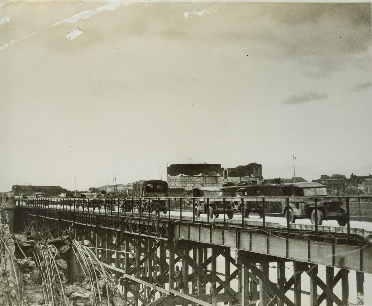 New Bridge for Old, 1/24/1944. Capua, Italy – When the Germans retreated across the Volturno River recently, they destroyed every bridge in the path of the Allied advance. As American troops reached the river, U.S. Engineers built pontoon bridges and then, when both sides of the river were in Allied hands built more permanent structures such as this bridge at Capua (above). Part of the structure of the old bridge can be seen at lower left.  Credit: (U.S. Signal corps photo from ACME);