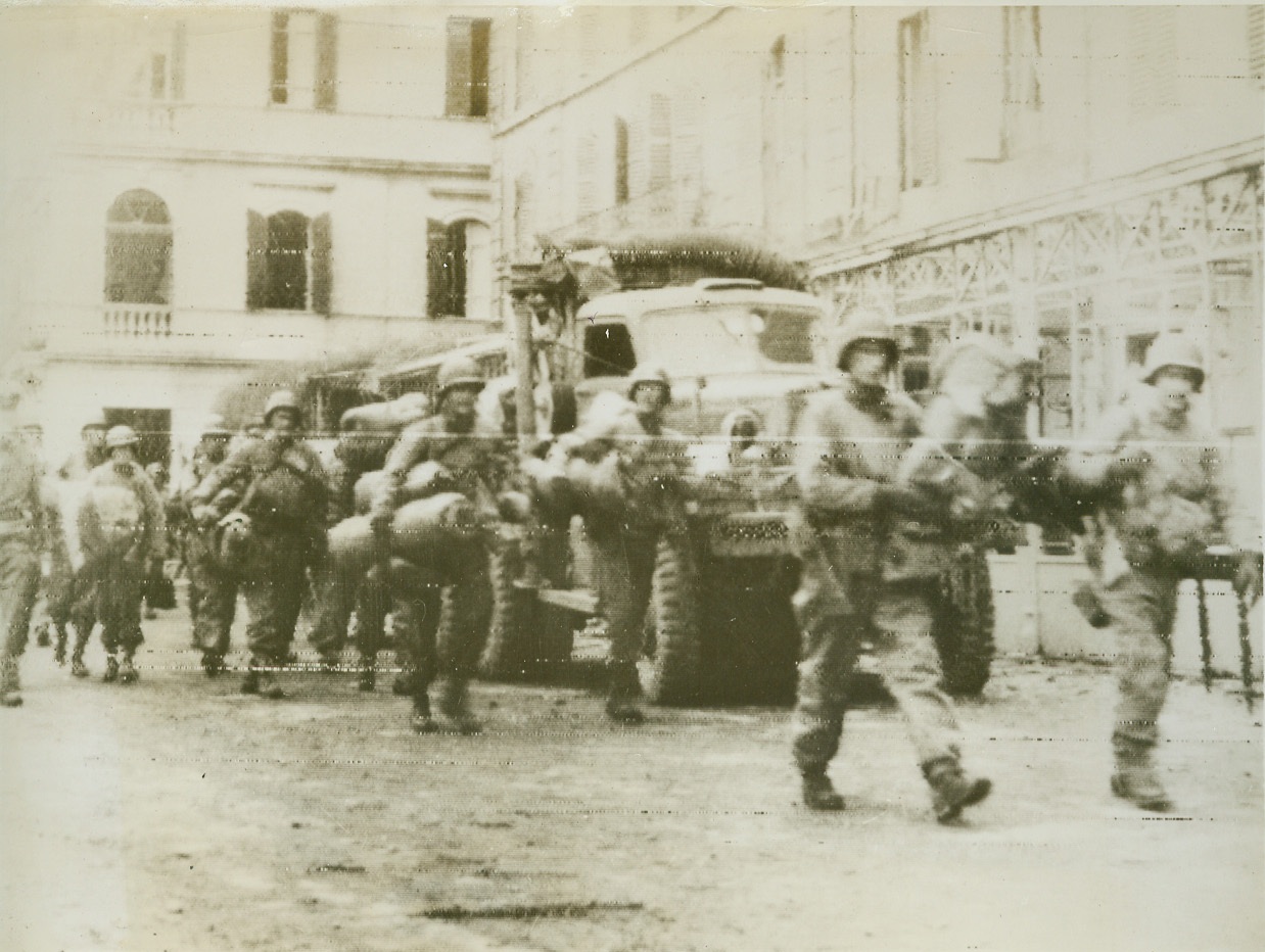 Reinforcements for March on Rome, 1/26/1944. Anzio, Italy – This photo, flashed to New York by radio tonight, shows American soldiers carrying bedrolls, as they marched through the coastal town of Anzio, to reinforce the Allied spearhead southwest of Rome. In the photo can be seen a truck bringing supplies from the newly-established beachhead south of Rome.  Credit: (Stars and Stripes photo thru OWI radiophoto from ACME);