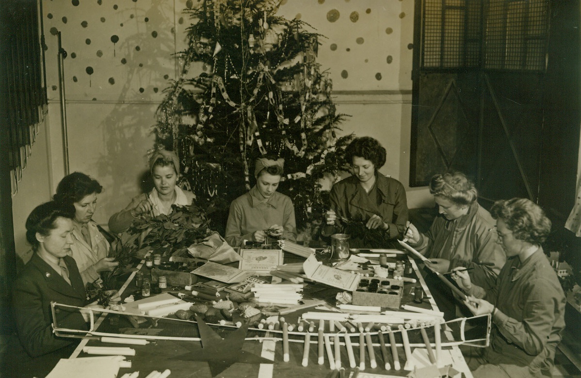 WAC Ingenuity Makes a Gala Christmas Tree, 1/4/1944. NORTH AFRICA – The nimble fingers of WACs in North Africa fashion cones, stars and paper chains, painting other ornaments in gay colors for their Christmas tree. (Left to right) Pfc. Iva Hess, of Washington, D.C.; Pvt. Marguerite Carnal, Dekalaba, Ill.; Corp. Theda McNall, Silver Spring, MD; Pfc. Mildred Ayers, Kosse, Tex.; Pfc. Ruth Ringenn, Peoria, Ill.; Lt. Sara Kruskall, Boston, Mass., and Pfc. Lucille Smith, of Milwaukee, Wisc.Credit: ACME photo by Charles Seawood, War Pool Correspondent;