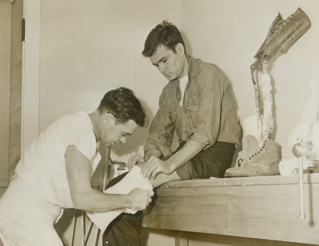 SO THE CRIPPED MAY WALK AGAIN, 1/20/1944. MARE ISLAND, CALIF.—S. C. Blankenship, ship cook 3/c of Alum Creek, W. Va., is fitted for an artificial leg by Pharmacist Mate J. J. McFado, an orthopedic technician, at the U.S. Navel Hospital, at Mare Island, Claif. The temporary leg on the shelf will enable the sailor to walk, barely six weeks after he had his leg amputated due to wounds received a Vella Lavella on December 2. Later, a plastic and steel leg will replace the temporary artificial one.Credit: Acme;