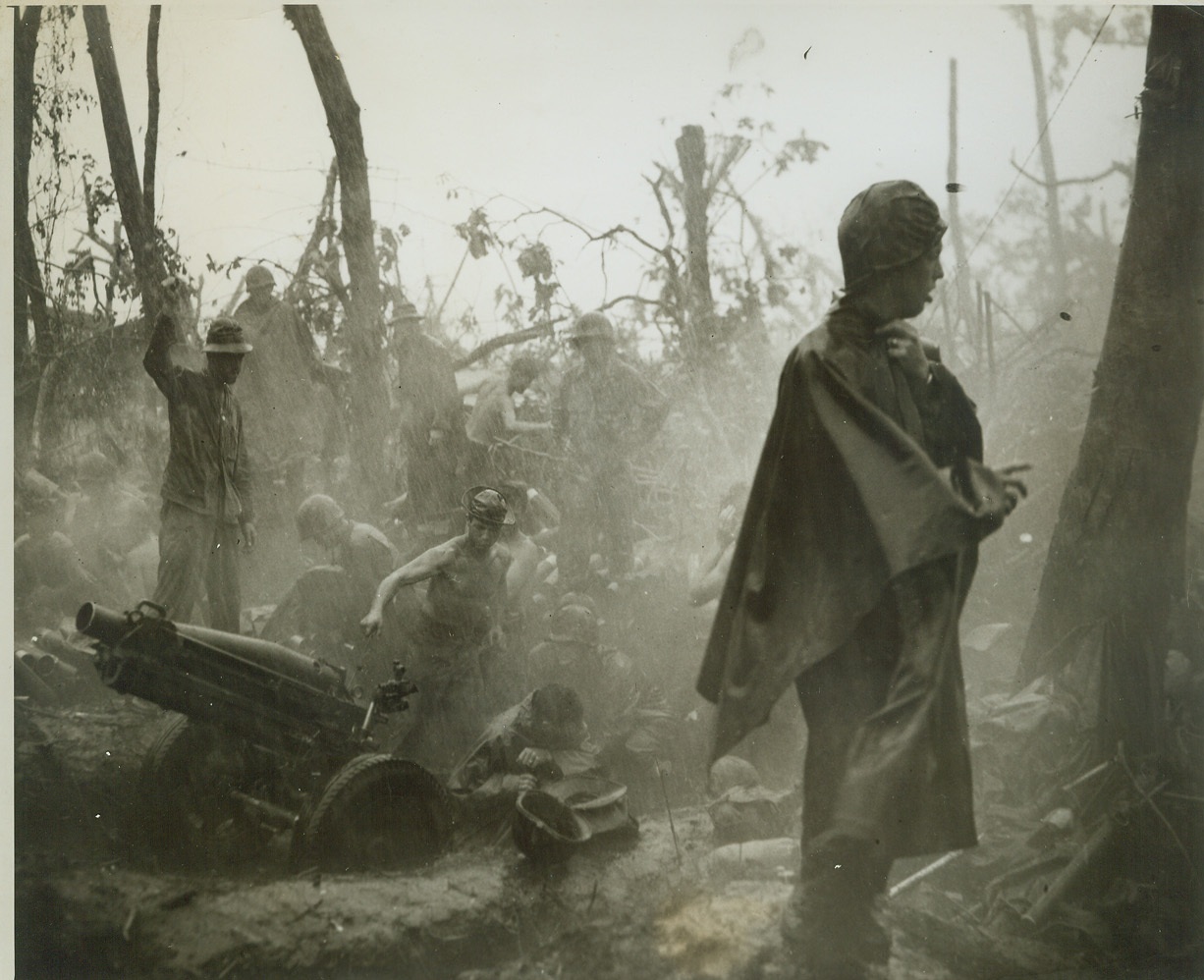 Fighting Through the Downpour, 1/18/1944. Cape Gloucester, New Britain – In spite of the tropical downpour that literally falls in sheets, drenching the fighters and their equipment, our Marines carry on in their battle for Cape Gloucester. His uniform plastered to his body, a Leatherneck gun crew member raises his hand to give the firing signal to men manning this 75mm Howitzer. Credit: -WP-(ACME Photo by Frank Prist, Jr., for the War Picture Pool);