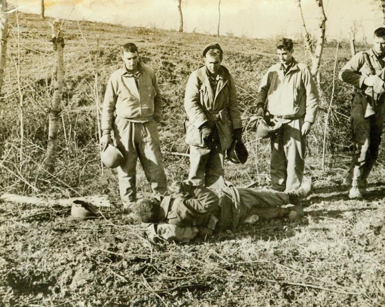 DEATH STRIKES THEIR BUDDY, 1/19/1944. ITALY – Fellow American soldiers doff their helmets before the dead body of an American engineer who was killed while removing a land mine. Note the hole in left foreground. He had been clearing a path through a mine field so that others could advance in safety. It exploded while he was working on it. Credit Line (ACME);