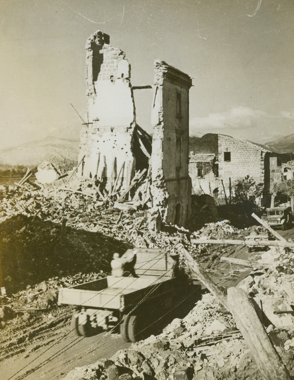 WAR HITS MIGNANO, 1/20/1944. ITALY—American units push their way forward over a blocked, devastated road in Mignano, Italy, now a mere remnant of a village on the way to Cassino. From the vantage point of the mountains in the background, the enemy keeps watch on our moves, and make fierce, brief counterattacks. Credit: Acme;