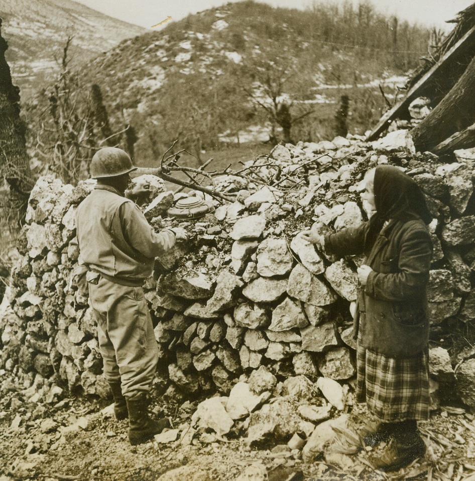 OLD ITALIAN WOMAN IS A VOLUNTEER SPY, 1/22/1944. ITALY—A wily old Italian woman who watched carefully as retreating Germans laid their mines in the village of Radicose, discloses the location of the deadly hidden weapons to Allied soldiers. Here, she point sout a mine carefully concealed in rocks. Credit: Acme;