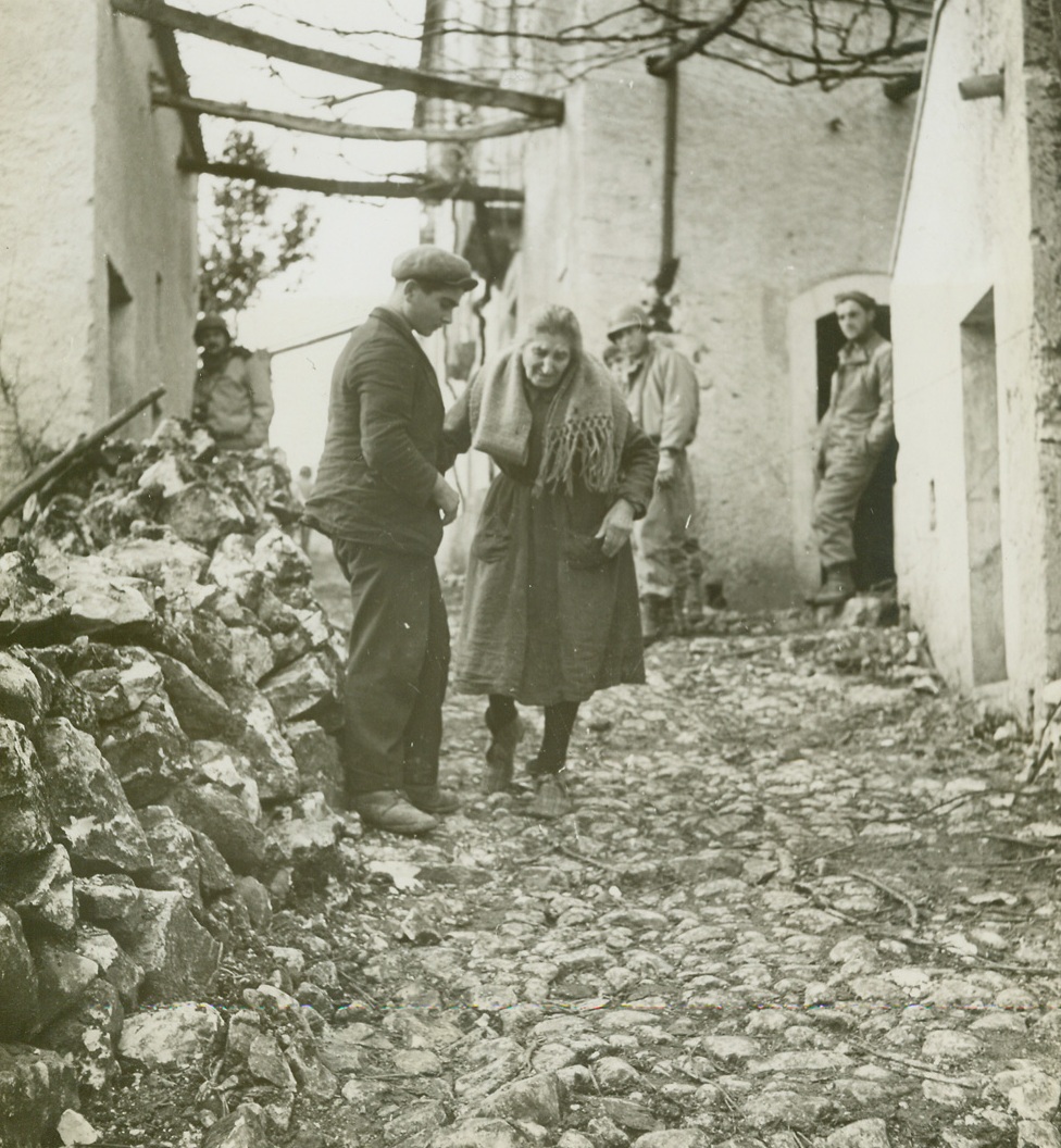 Return of the Natives, 1/1/1944. LAGONE, ITALY—An Italian boy helps his feeble grandmother along the rocky, rubble-strewn street that leads to their bomb-wrecked home, which was completely destroyed by the retreating Nazi forces. Credit:  ACME photo by Bert Brandt, war picture pool correspondent.;