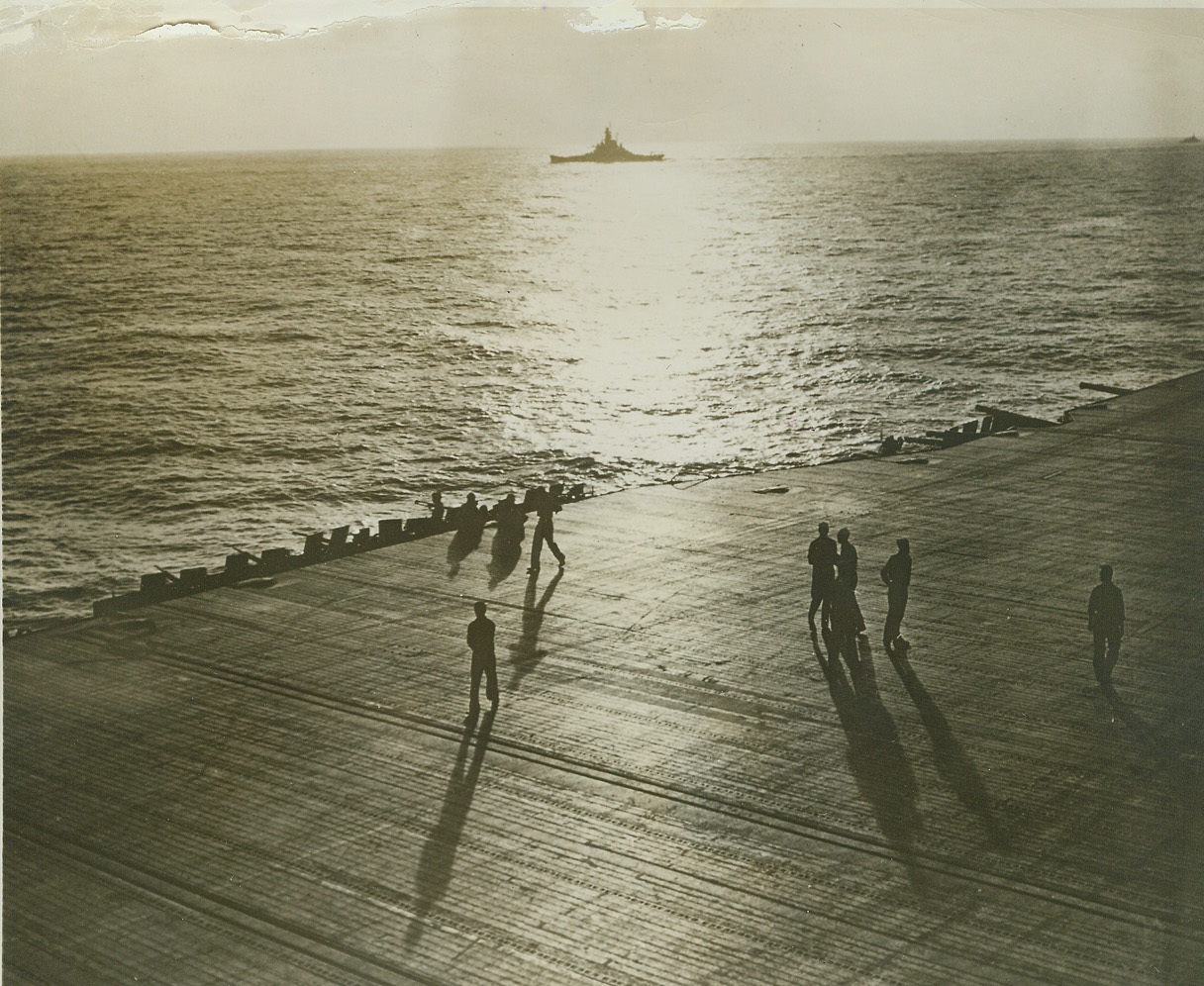 Champion Team of the Sea, 1/28/1944. Late afternoon sunlight slants across the flight deck of a 25,000-ton Essex Class aircraft carrier while, in the distance, a modern U.S. Navy battleship of the 35,000-ton South Dakota Class steams along on a task force mission somewhere in the Central Pacific. For the first time, the Navy has released combat pictures of the powerful new combat teams of carriers and battleships which are seeking out the Jap enemy. Credit (Official U.S. Navy Photo from ACME);
