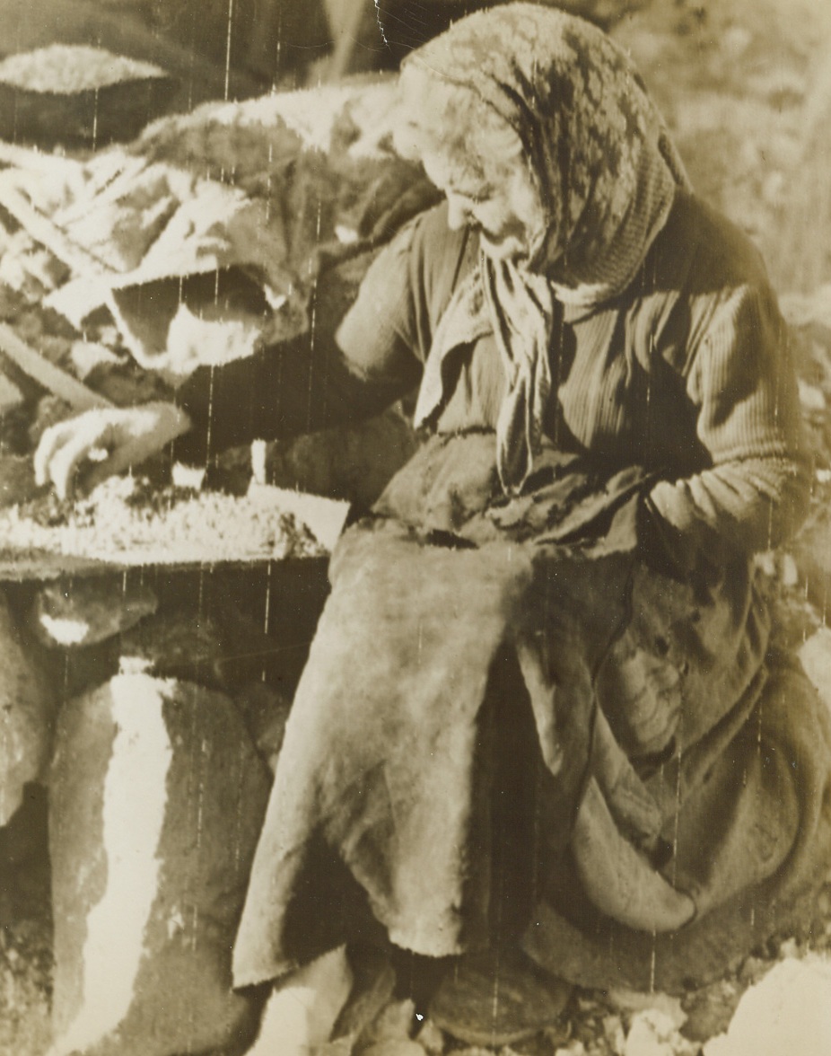 Bits of Food – Her Dinner, 1/19/1944. SAN PIETRO, ITALY—An aged Italian grandmother beated amid the ruins of her home in San Pietro, separates bits of food from dust and rubble, trying to gather enough for a meal. San Pietro was the scene of some of the bloodiest fighting of the whole Italian campaign. Today, Allied troops have crossed the Garigliano River and have set up a solid bridgehead on the north bank. Credit: ACME PHOTO by Bert Brandt for the War Picture Pool via Army Radiotelephoto.;