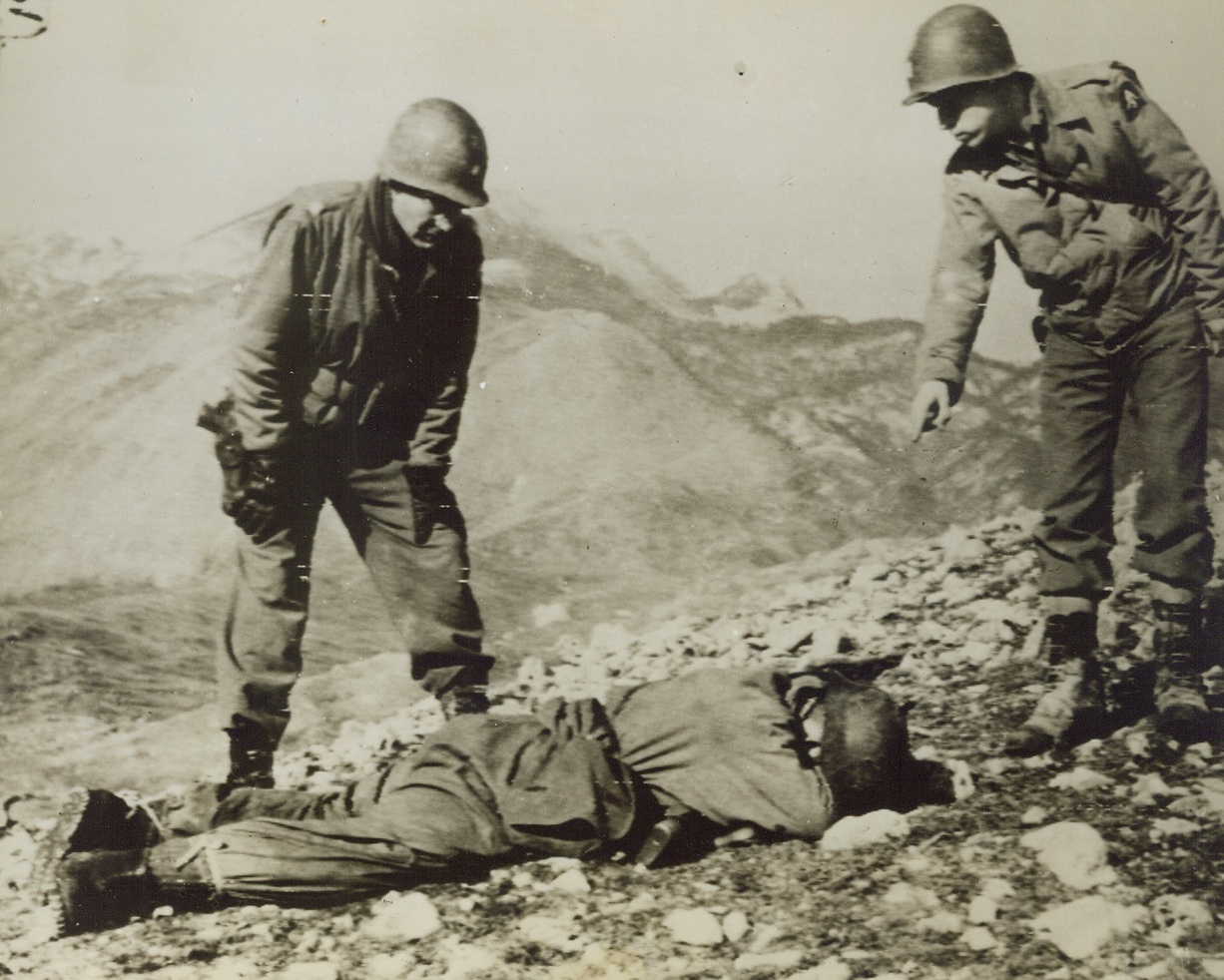 DEATH ON THE ROAD TO ROME, 1/18/1944. CERASUOLO, ITALY—His fleeing comrades left this German soldier to be buried by the Allies, as the Nazis beat a hurried retreat in the Cerasuolo area. The dead German was found by Lt. Col. H. I. Ketchum (left) of Abbottsford, Wisc., and Captain R. L. Johnson, of a field artillery battalion, who were on a reconnaissance mission.Credit: Signal Corps Radiotelephoto from Acme;