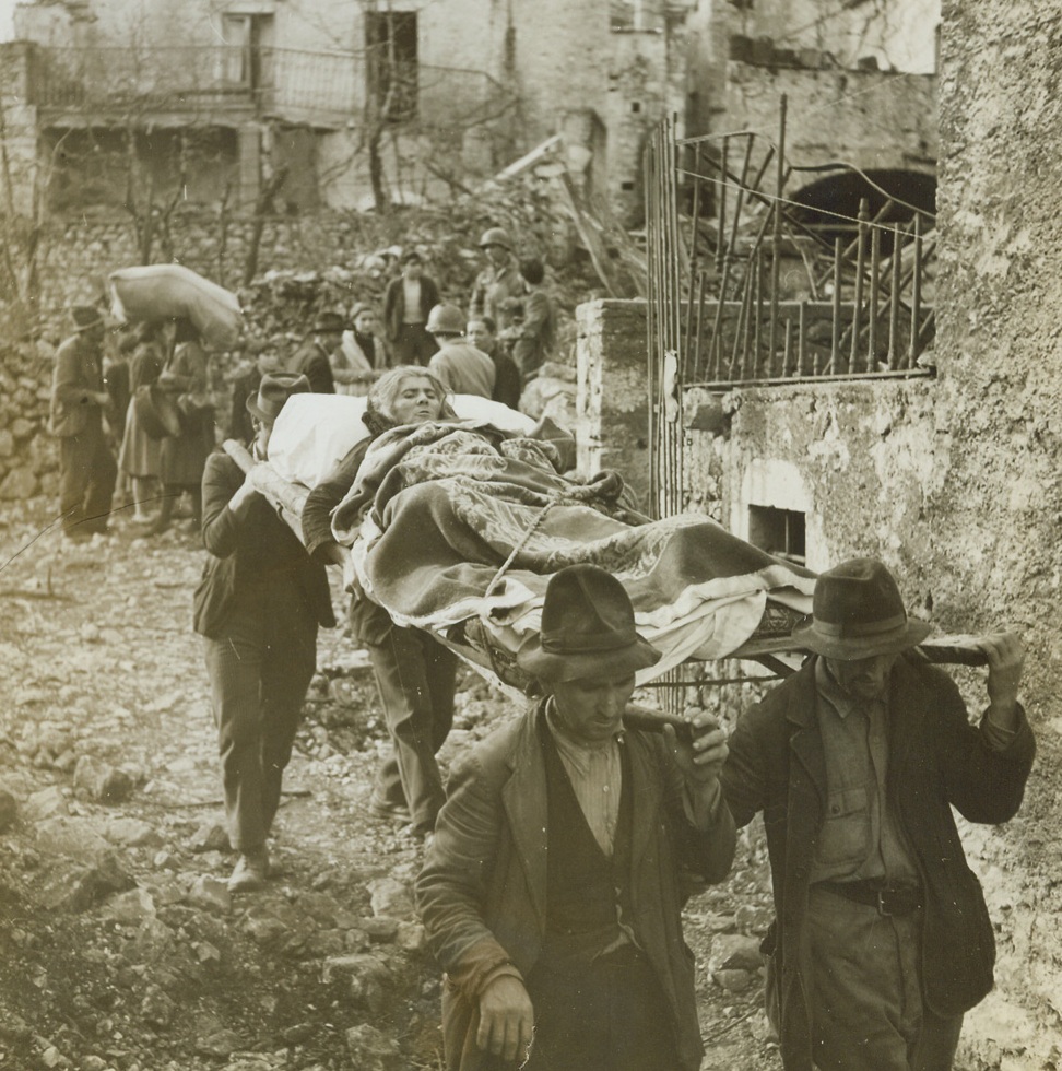 Return of the Natives, 1/1/1944. LAGONE, ITALY -- Scene of many days of bitter fighting, the tiny mountain town of Lagone fell to warriors of Lt. Gen. Mark Clark's Fifth Army, and the smoke of battle had hardly cleared before hundreds of natives flocked down from the hills to return to their homes. The pathos of their tragic homecoming to the wrecked, blasted buildings is recorded in this series, made by Acme correspondent Bert Brandt, for the War Picture Pool. Non-combatants all these men, women and children find that war is a very personal experience nevertheless: an experience that has left them with a deep, grim hatred for the Germans. New York Bureau Members of her family carry an old woman down from the hills on a crude stretcher. The woman's face mirrors the agony that the bumpy journey caused her. Credit - WP - (Acme Photo by Bert Brandt, War Pool Correspondent);