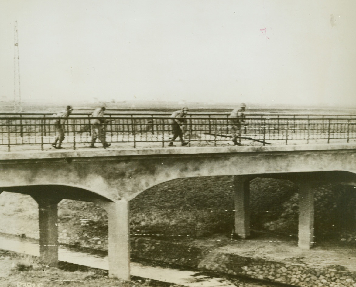 A treacherous bit of Road Toward Rome, 1/29/1944. NETTUNO, ITALY – With good reason, a Fifth Army infantry patrol feels alone and unprotected as it crosses a bridge over Mussolini Canal that leads into German territory. It’s a bit of action that may never go down in history but these men will remember it all their lives. Credit (Acme Photo by Bert Brandt, via Signal Corps Radiotelephoto);